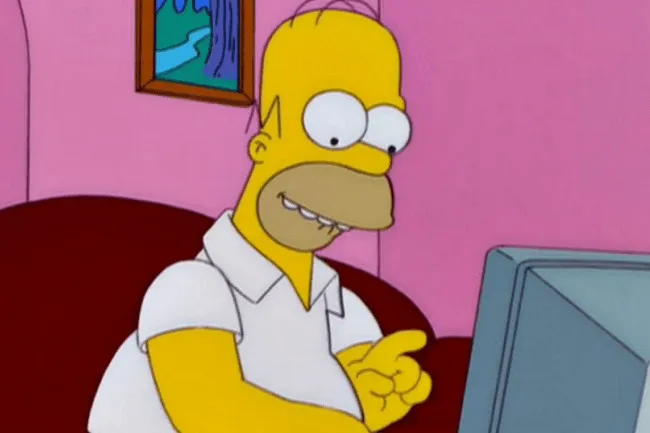 Homer Simpson sitting on a couch, pointing at a computer screen with a pink wall and framed picture in the background.