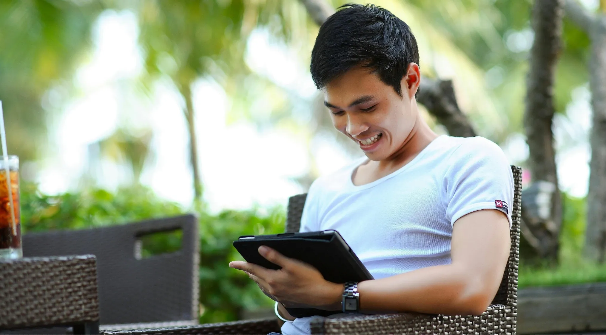 Young man smiling while taking a language quiz on a tablet outdoors, testing knowledge of Standard English and punctuation.