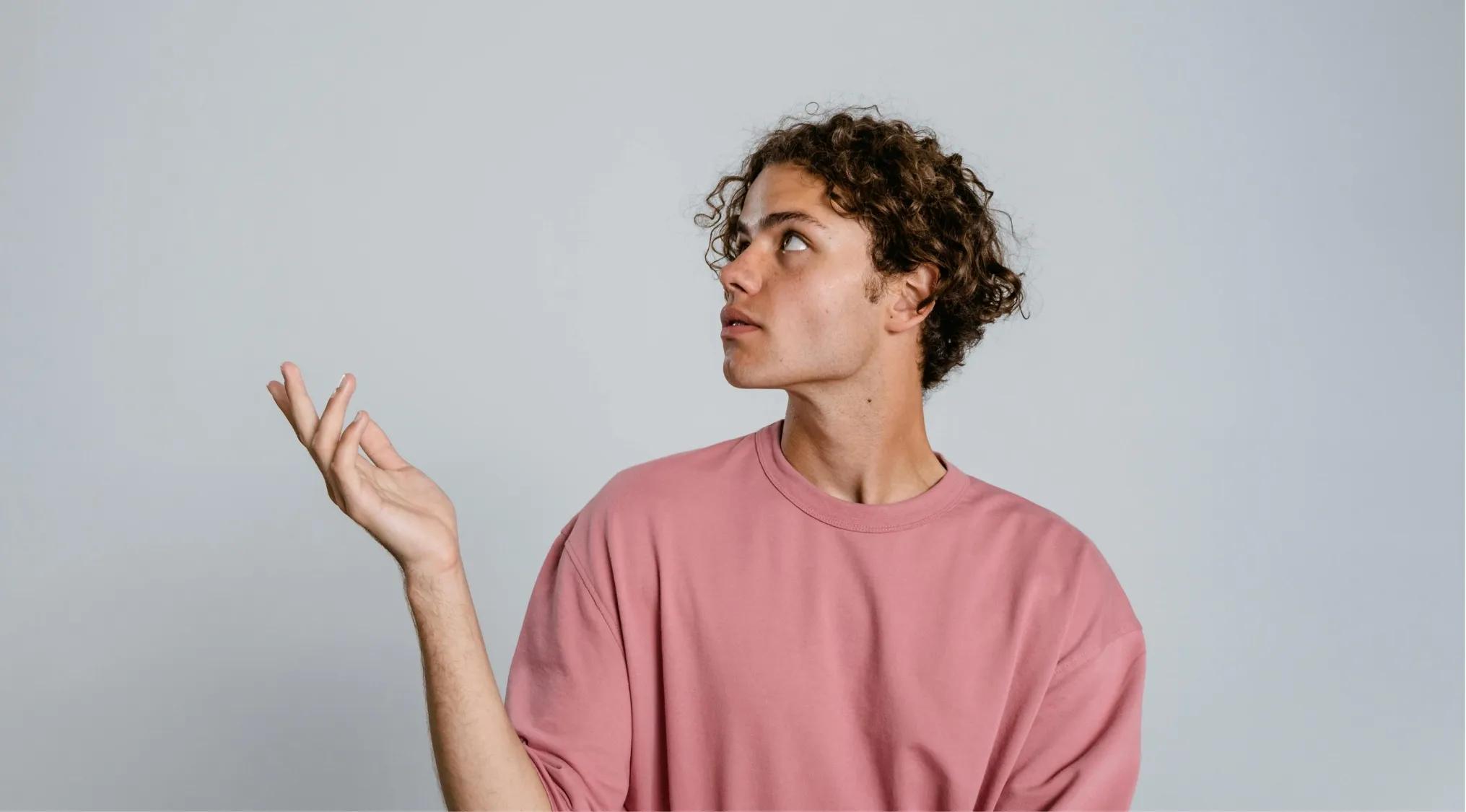 Young man in a pink shirt looking up thoughtfully, representing a language quiz about correct comparative usage.
