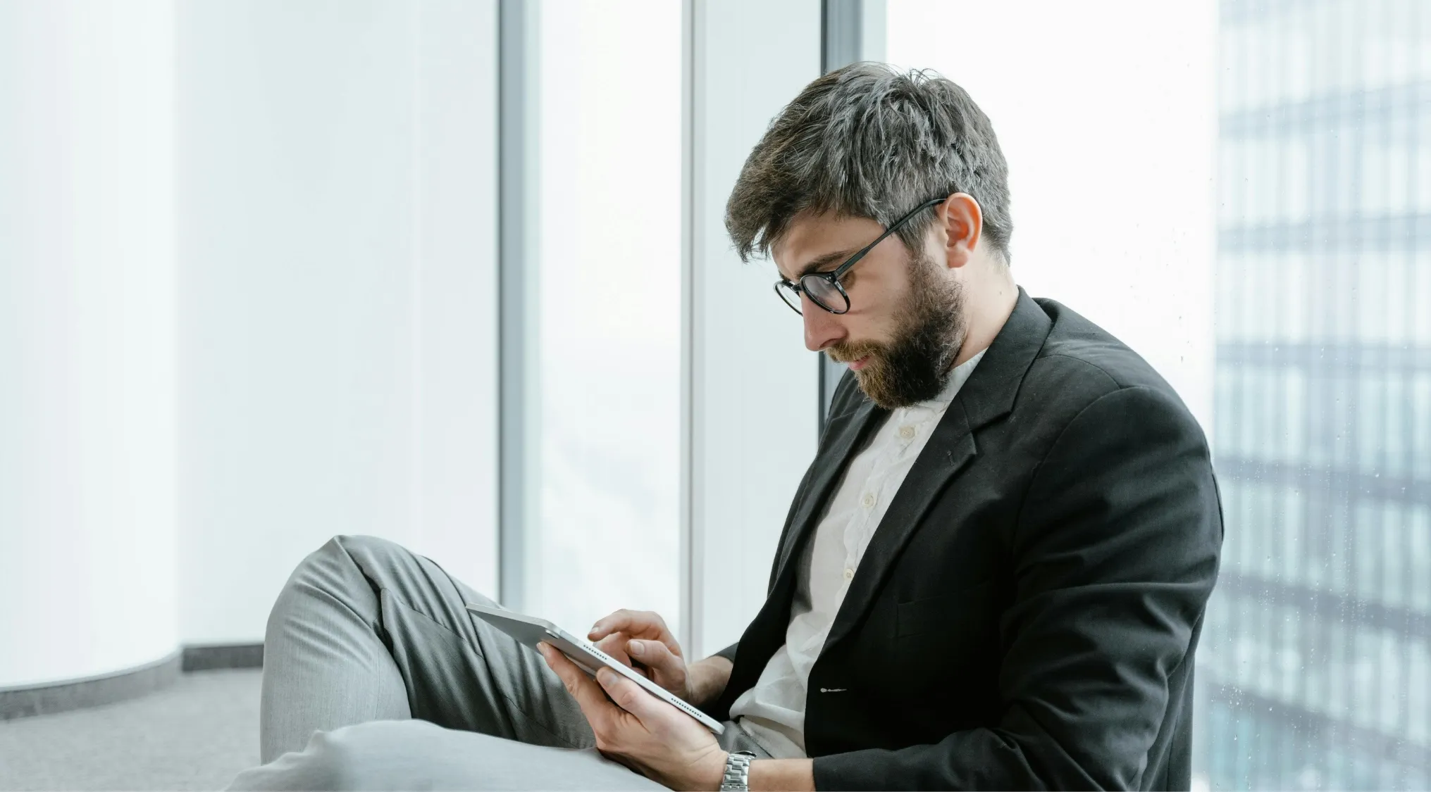 Man in glasses reading on tablet while sitting by window, focused on a language quiz about idioms and literature.