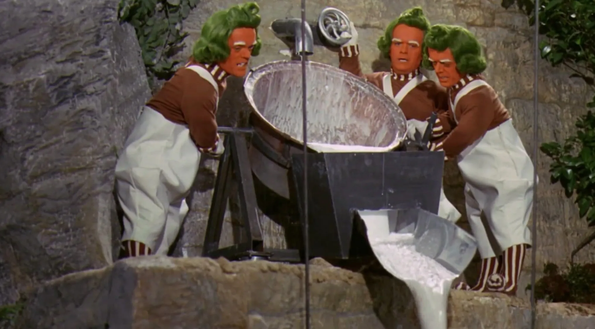 Three 70s movie characters with green hair and white overalls pouring white liquid in a factory setting.