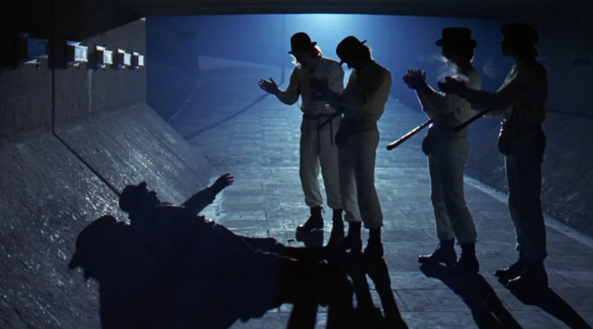 Group of men in bowler hats and white clothes standing in a dark tunnel in iconic 70s movie scenes.