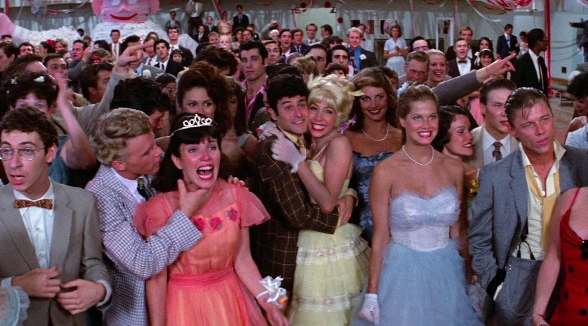 Crowded dance scene from a 70s movie with people dressed in retro prom outfits and lively expressions.