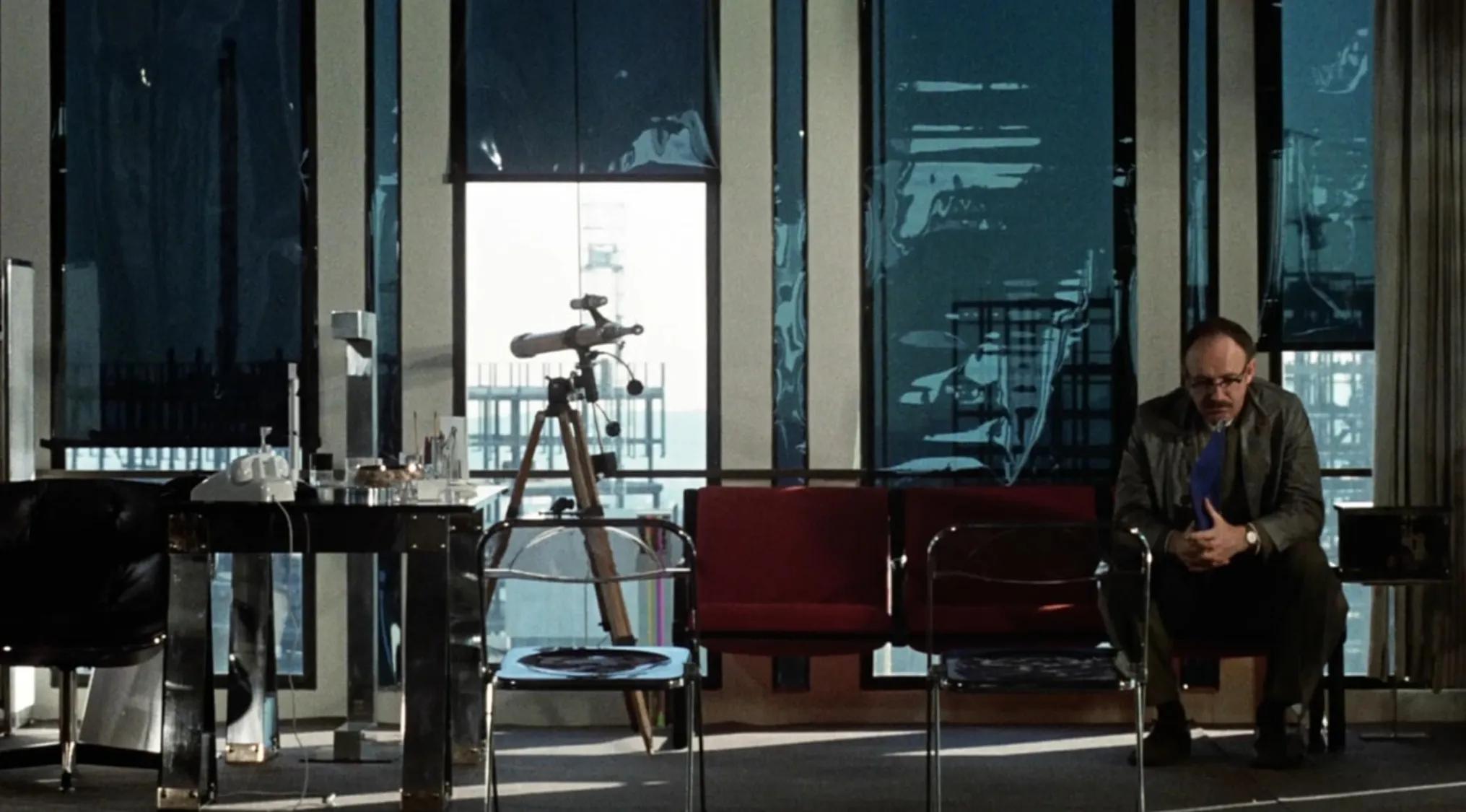 Man sitting in an office with a telescope and chairs, a scene from a 70s movie for you to uncover the film name