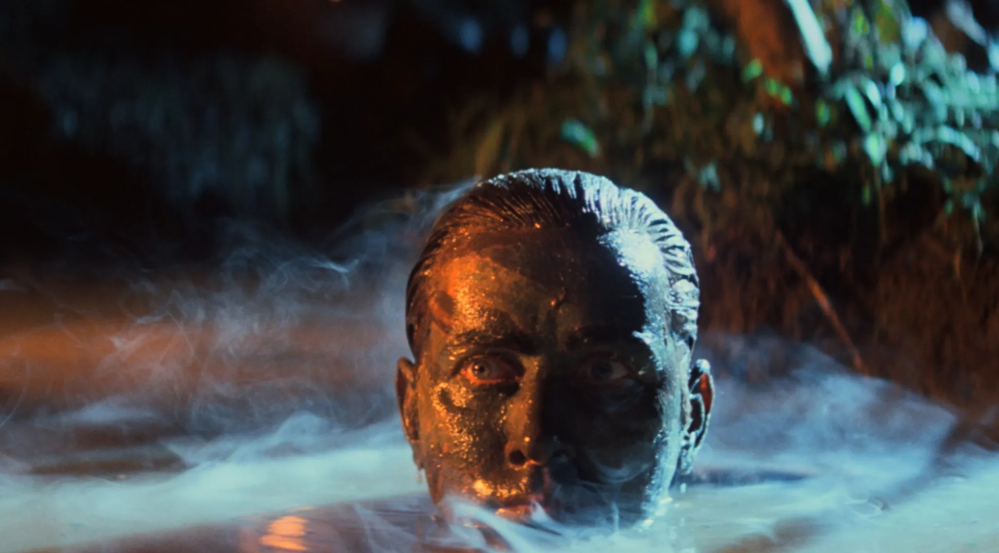 Close-up of a man emerging from water with smoke surrounding him in a dramatic 70s movie scene.