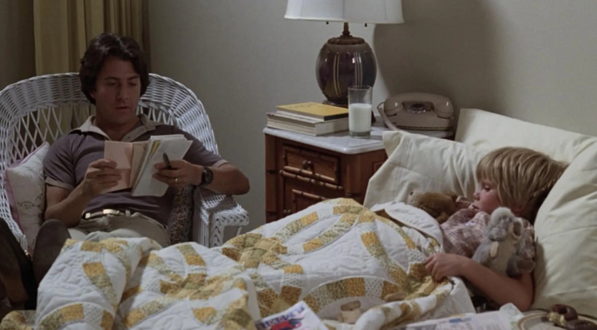 Man sitting reading by a bedside while a child lies under a quilt with stuffed animals in a 70s movie scene.
