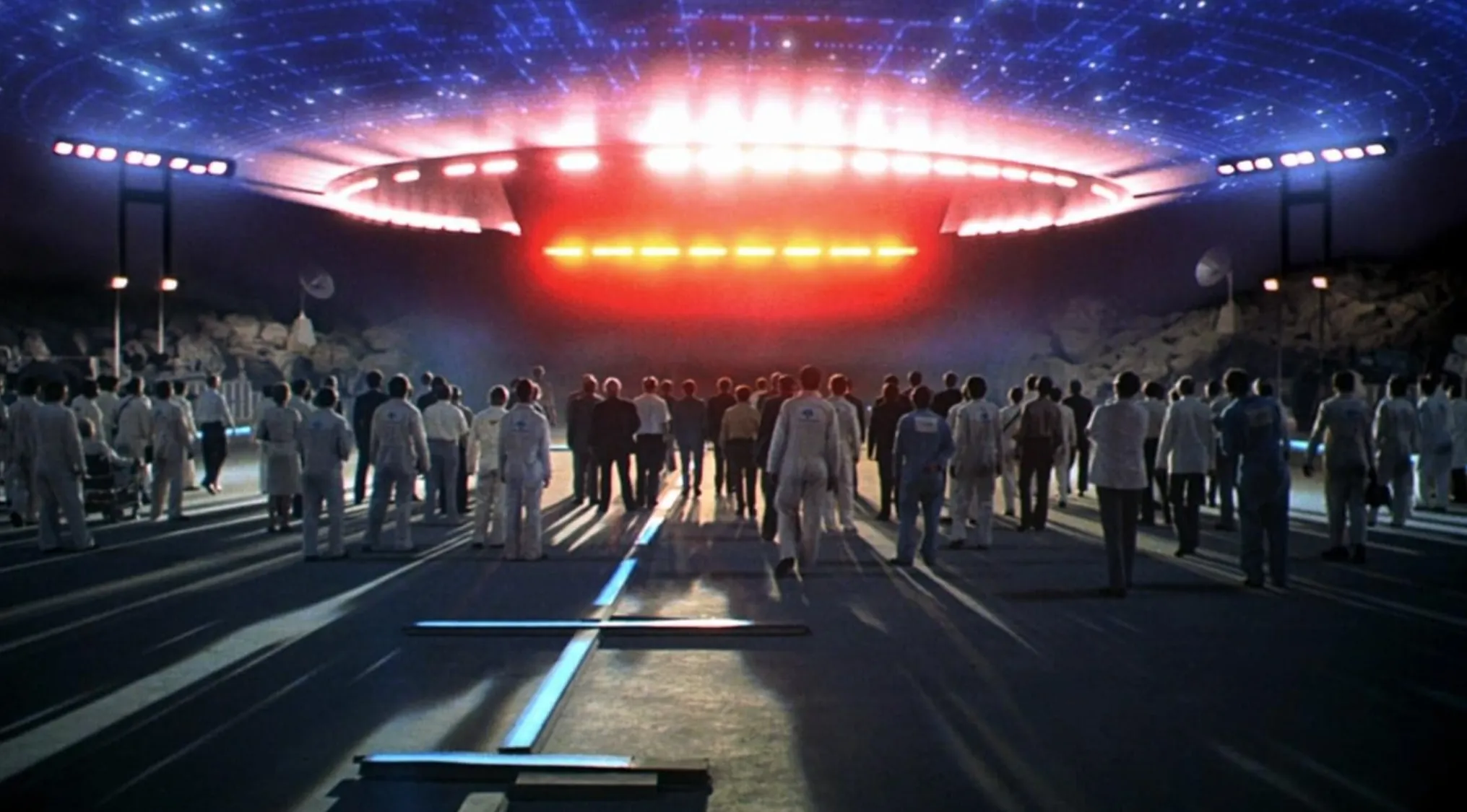 Crowd in white suits approaching bright lights of a large spaceship in iconic 70s movie sci-fi scene.