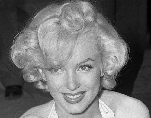 Marilyn Monroe smiling with curled blonde hair, iconic style symbol of the 1950s Hollywood era.