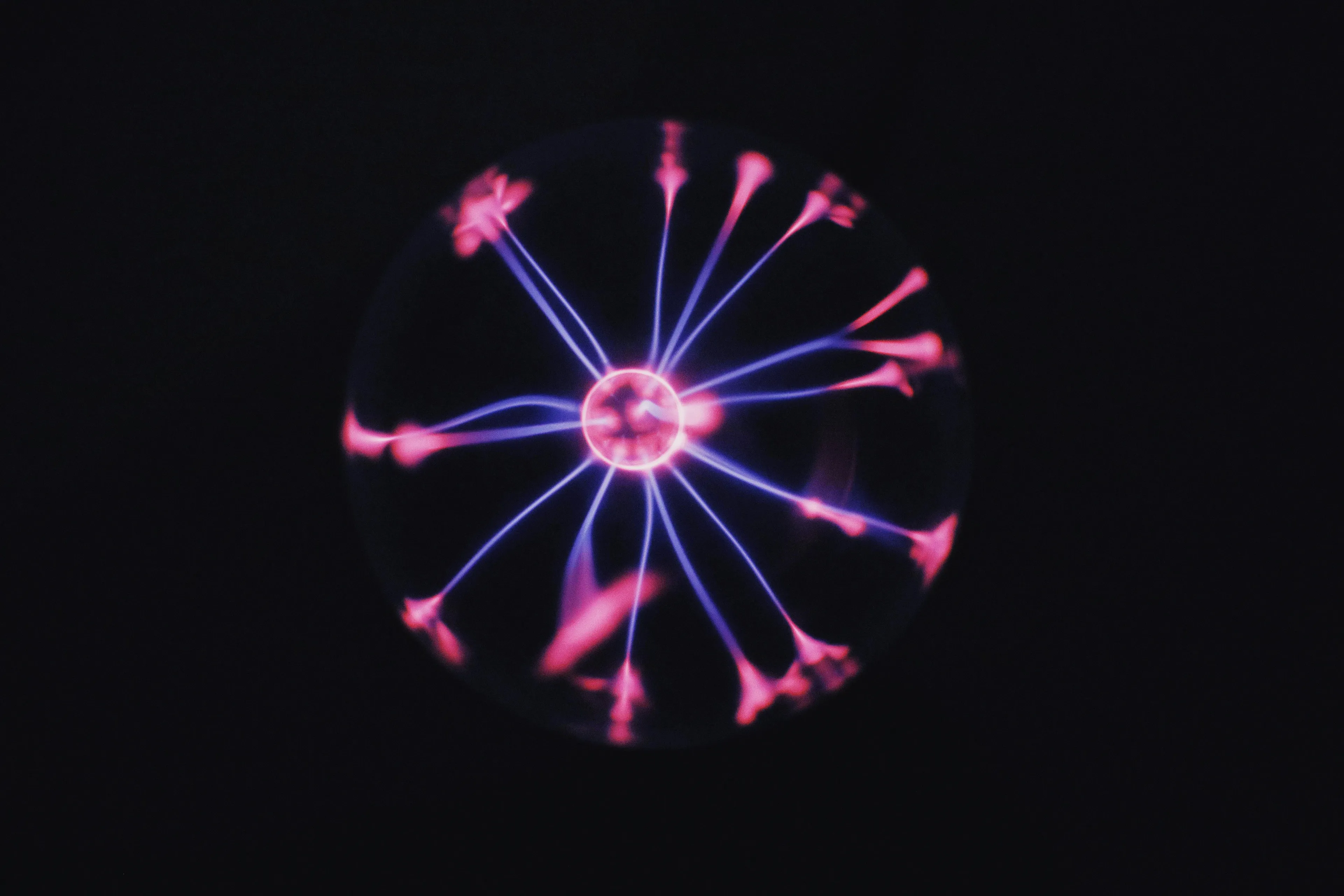 Plasma globe with pink and purple glowing electric filaments illustrating the center of an atom concept for pub quiz.