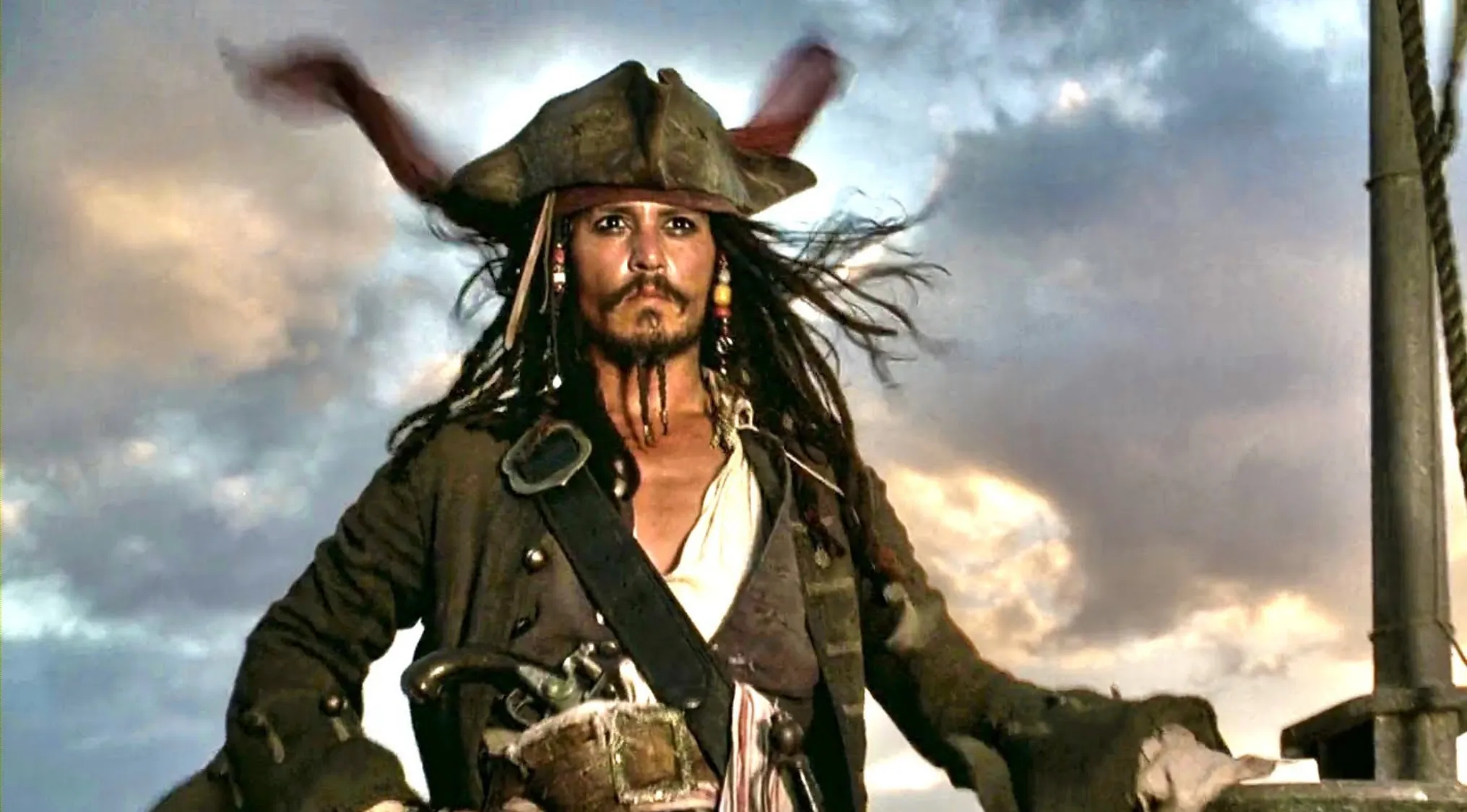 Image of Captain Jack Sparrow from Pirates of the Caribbean, wearing pirate attire on a ship at sunset.