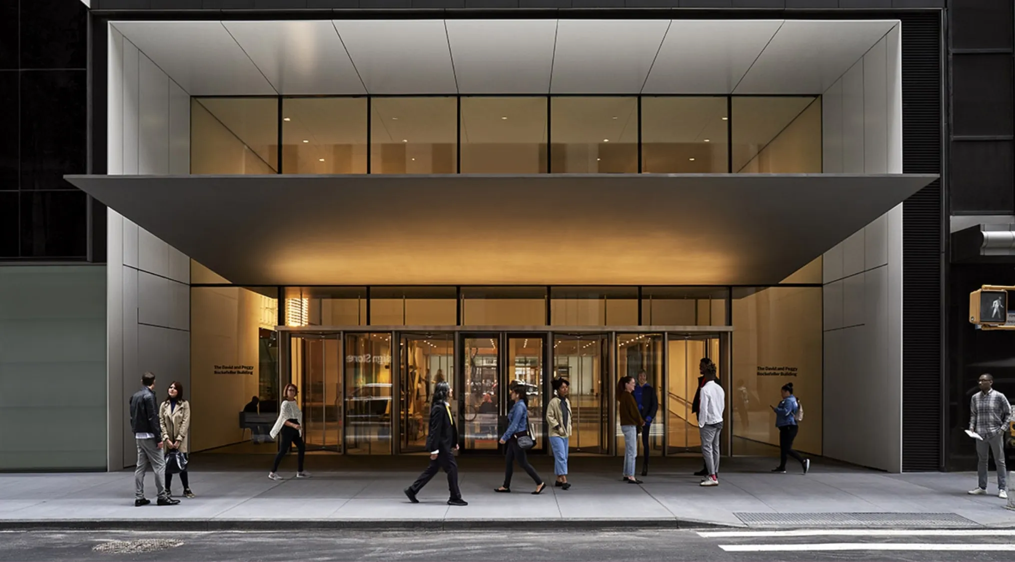 Entrance of the Museum of Modern Art MoMA in New York with people walking and standing outside the building.