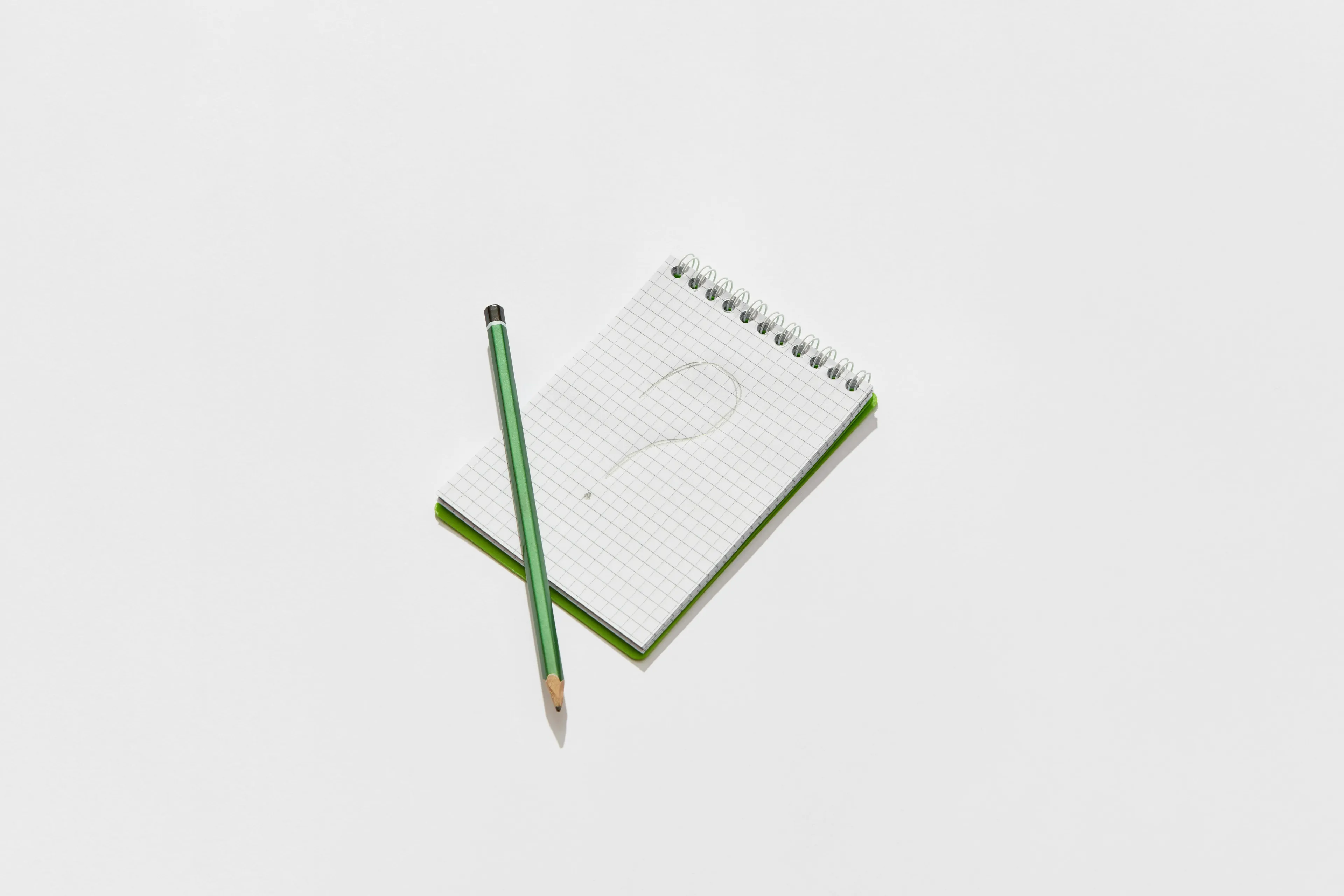 Green pencil resting on a grid notepad with a question mark, symbolizing art knowledge and drawing questions.