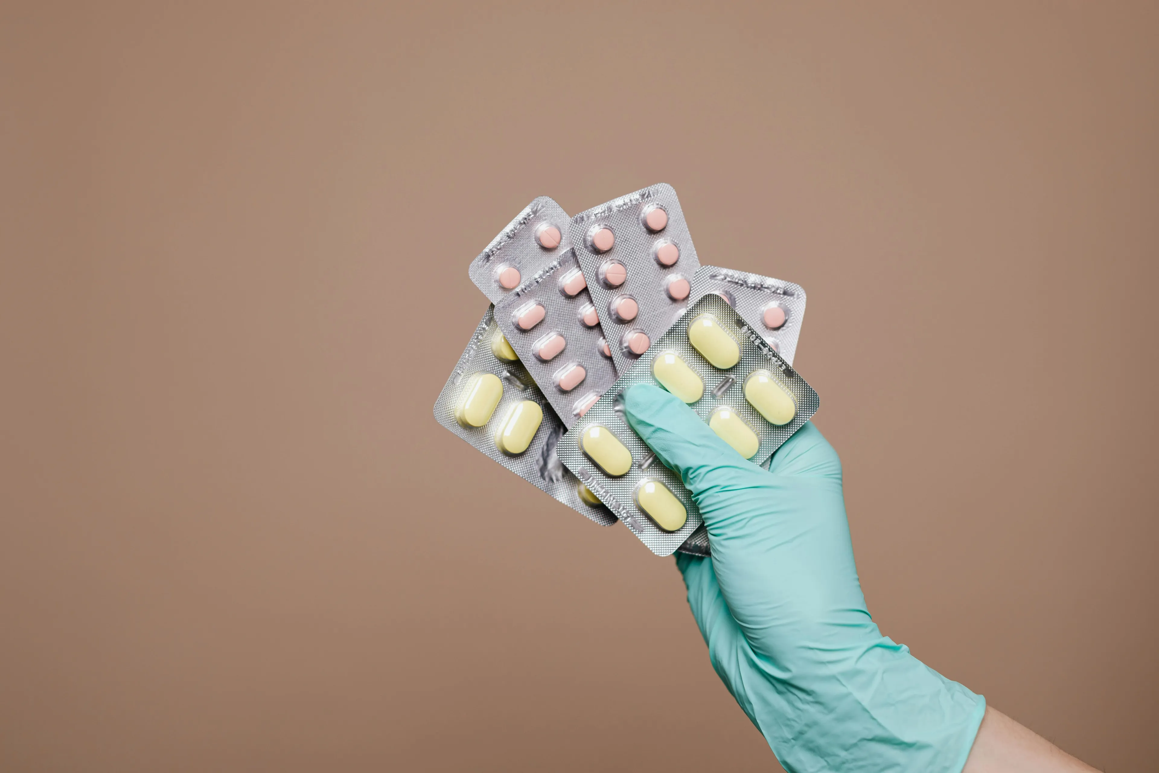 Hand in medical glove holding multiple antibiotic blister packs against plain background for common cold quiz.