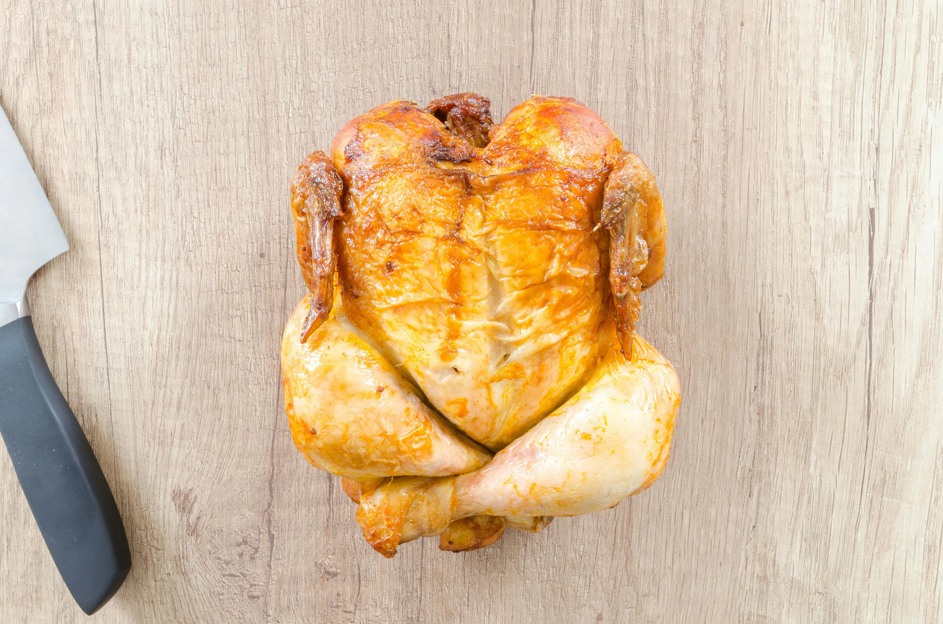 Roasted whole chicken on a wooden surface next to a knife highlighting minimum internal temperature chicken safe.