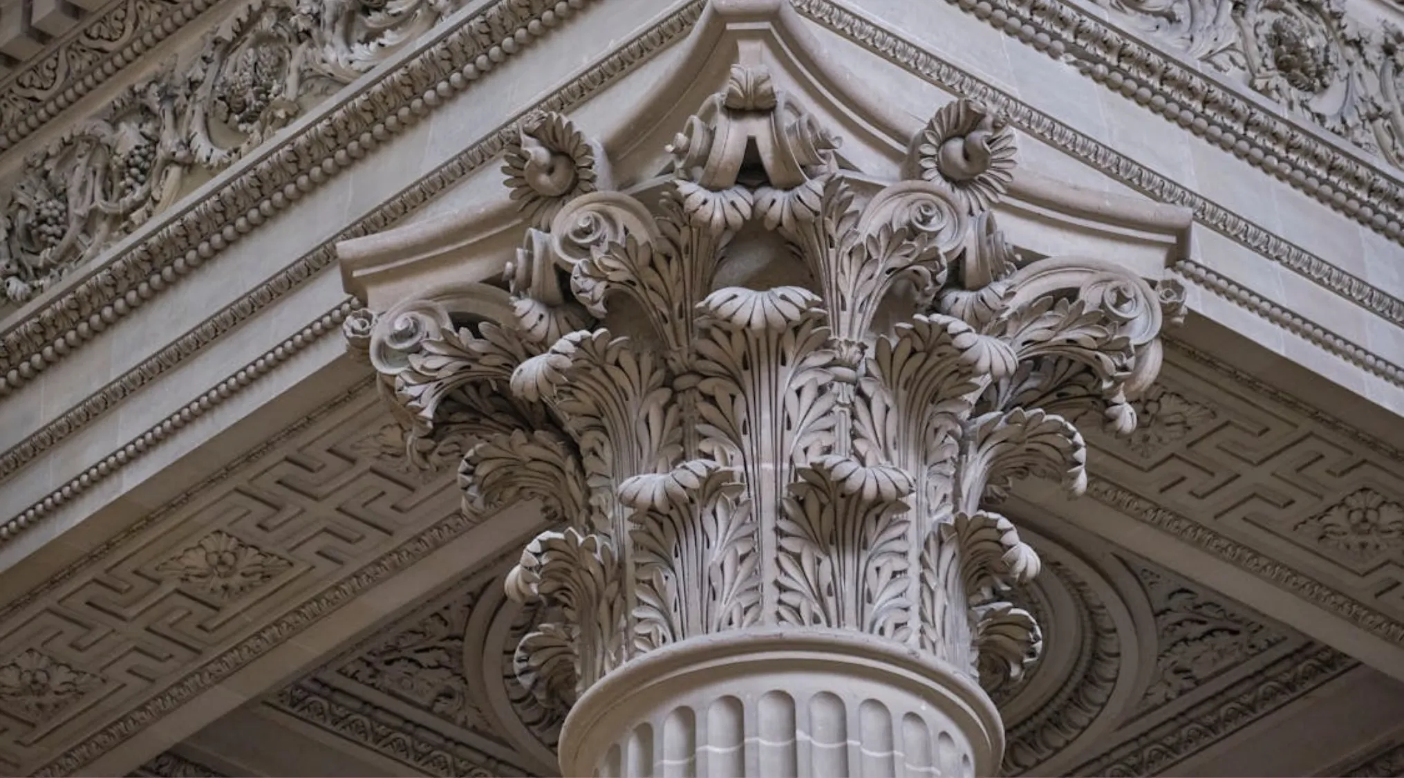 Close-up of an ornate classical column capital featuring detailed acanthus leaf carvings in classical art.