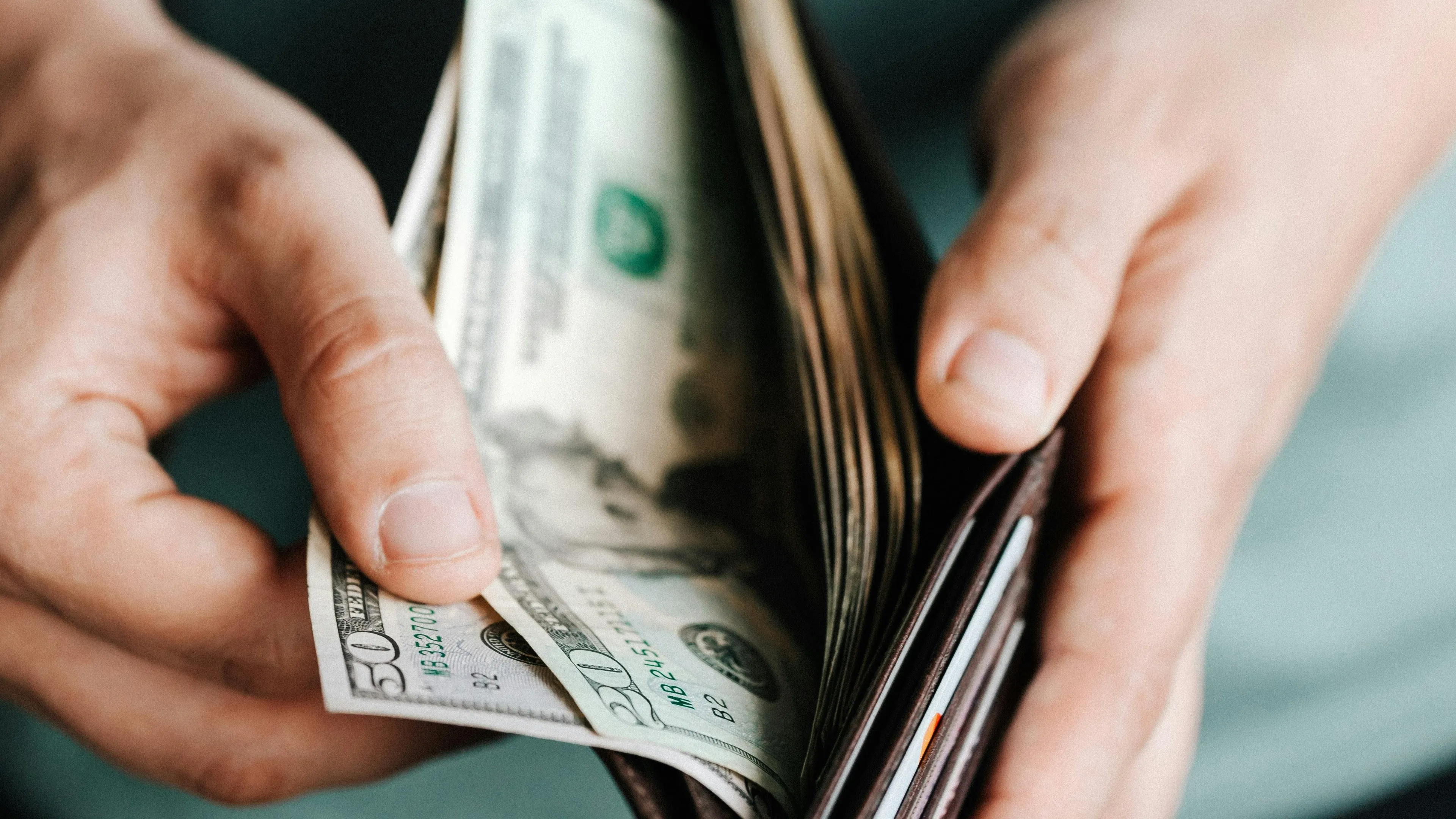 Hands holding a wallet with US dollar bills, illustrating the concept of gross and net salary differences.