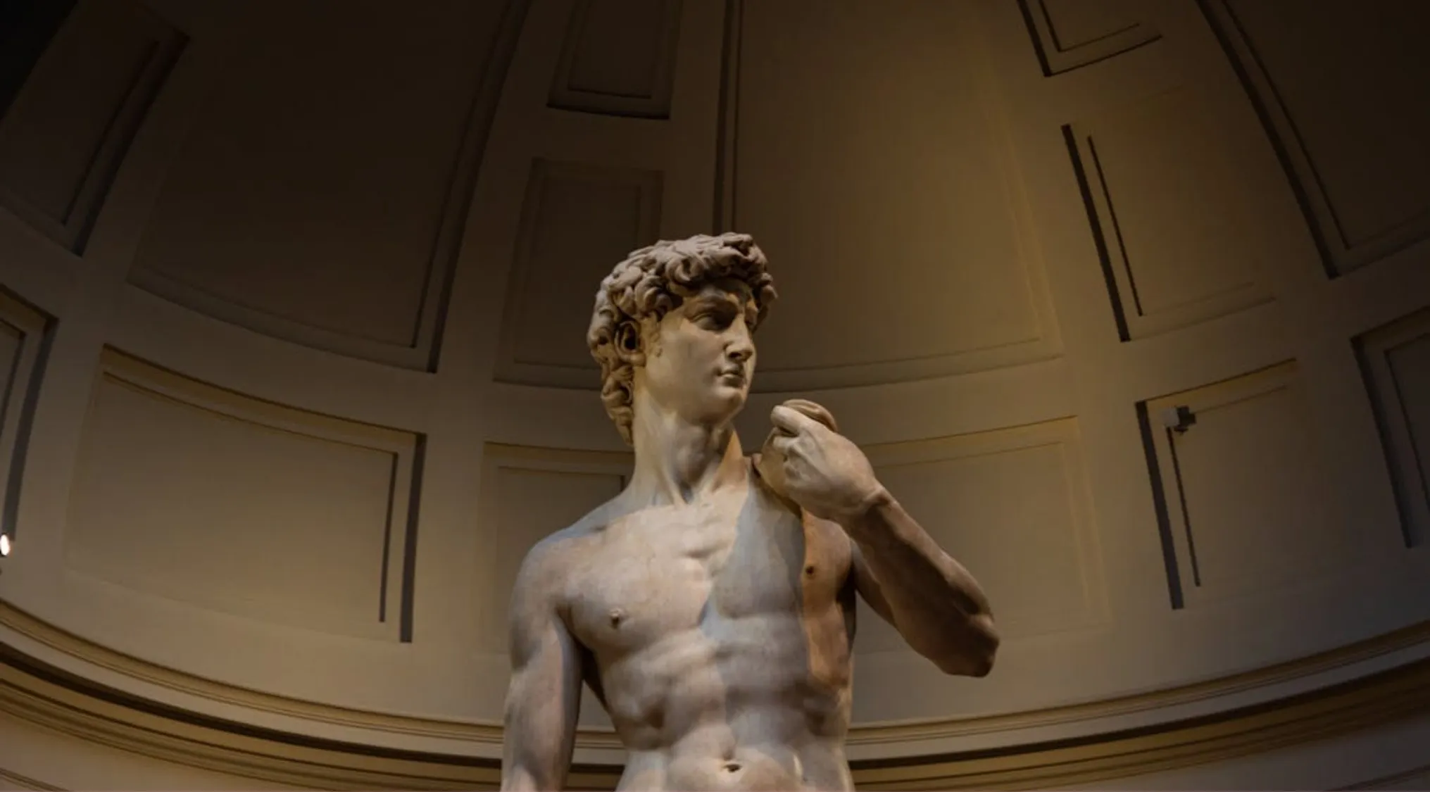 Marble sculpture of a male figure displayed inside a museum with detailed anatomy and artistic craftsmanship.