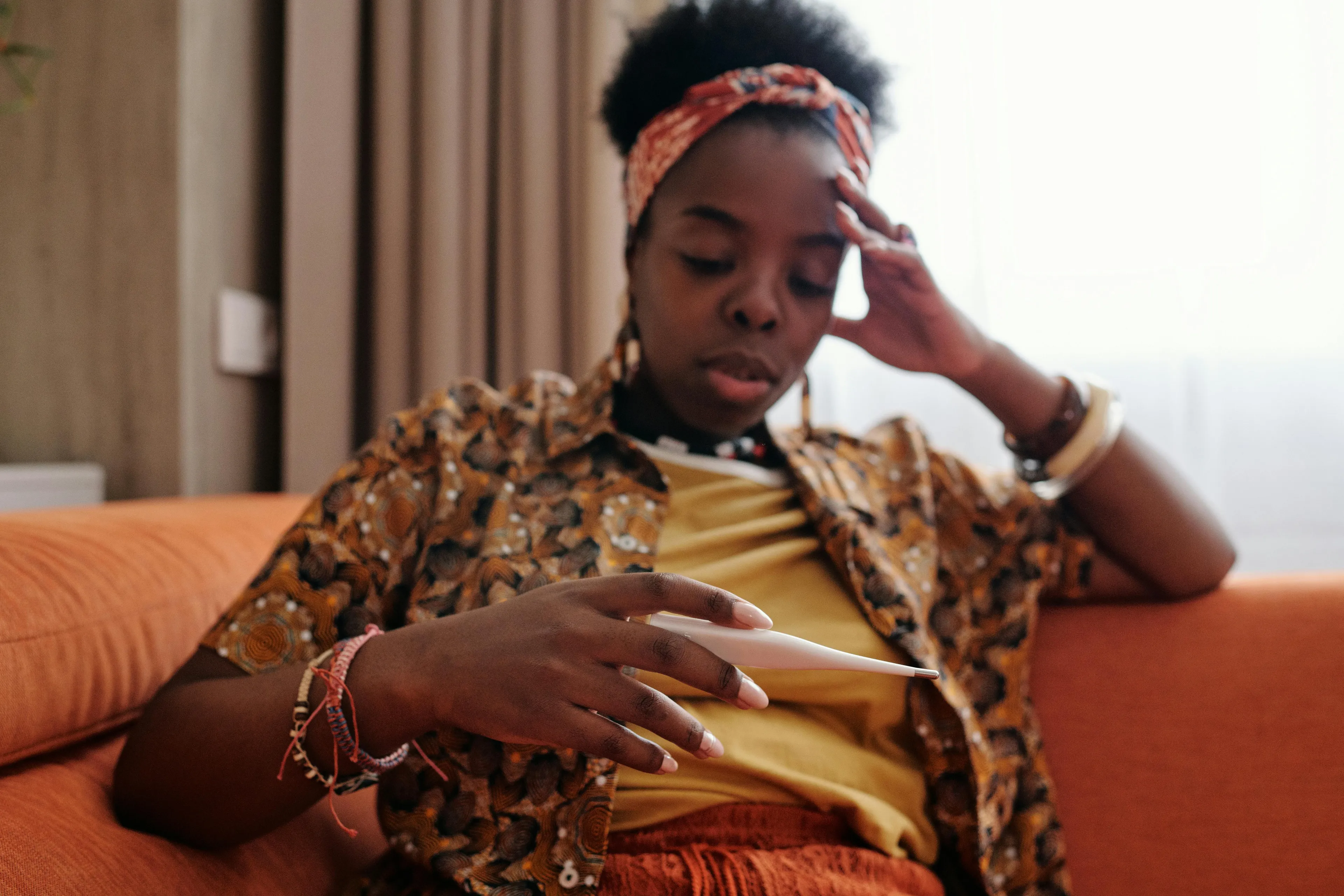 Woman sitting on couch checking thermometer, illustrating body temperature and when a fever needs a doctor call for adults.