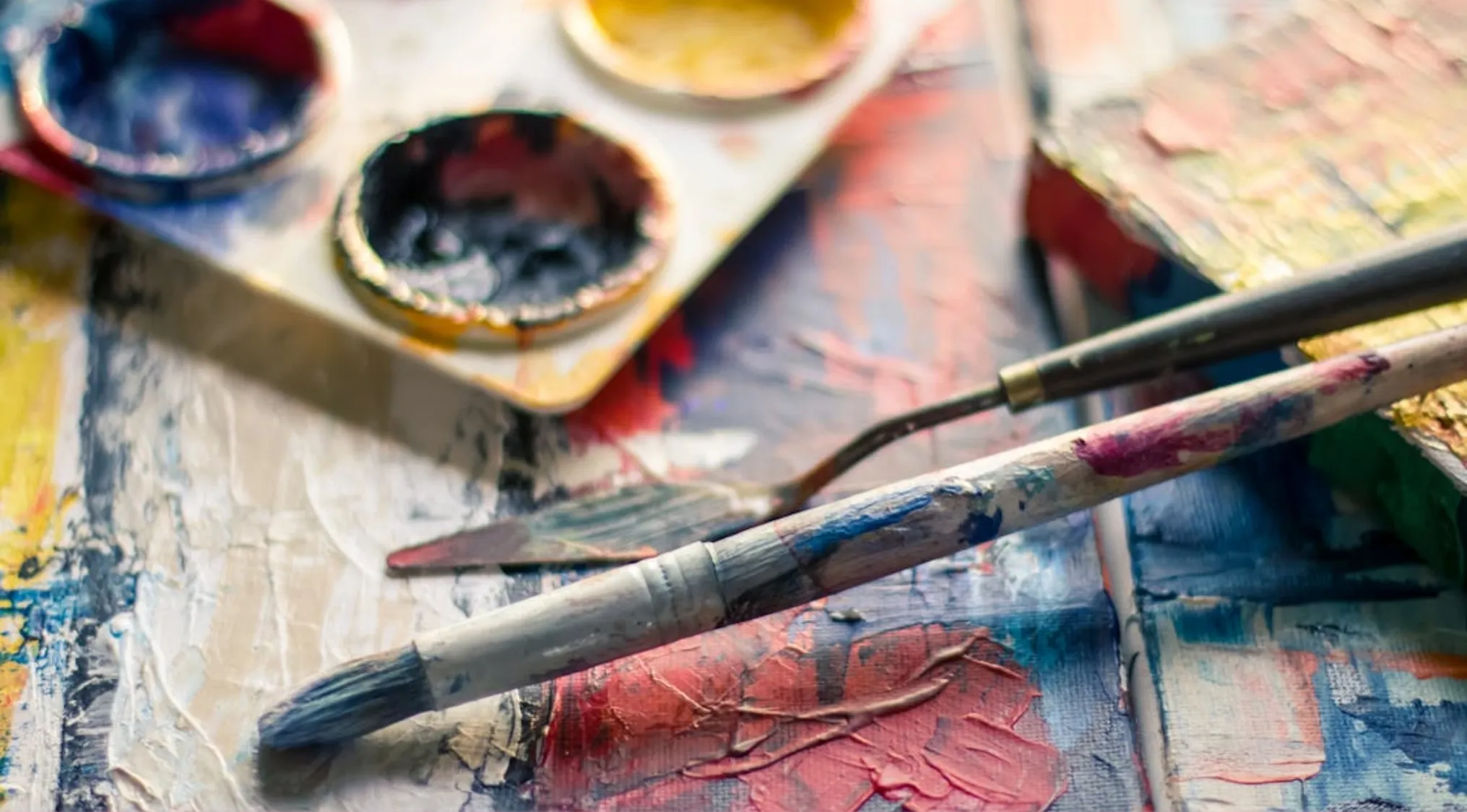 Close-up of paintbrushes and palette knife resting on vibrant mixed paint illustrating tertiary colours in art.