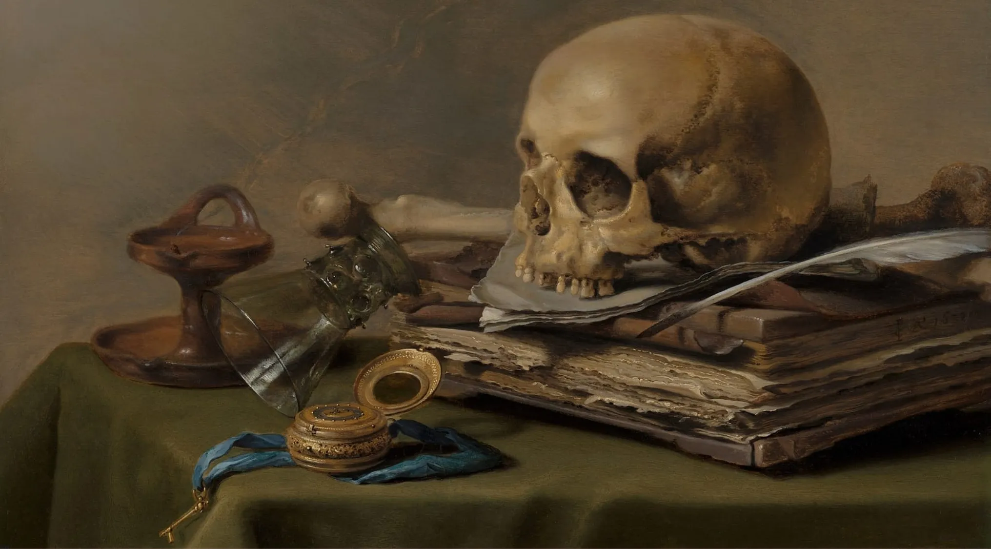 Still life painting setup with skull, old books, feather, and antique objects on a green cloth background.