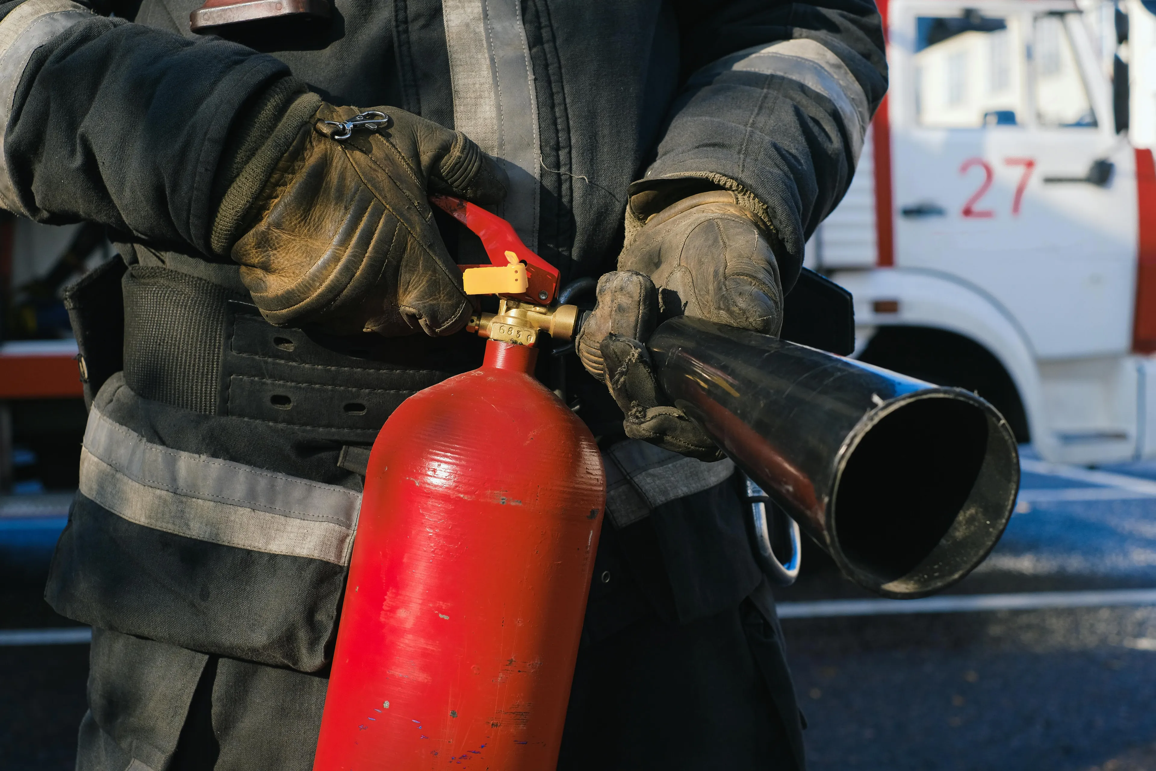 Firefighter in protective gear holding a red fire extinguisher designed for electrical fire safety use.