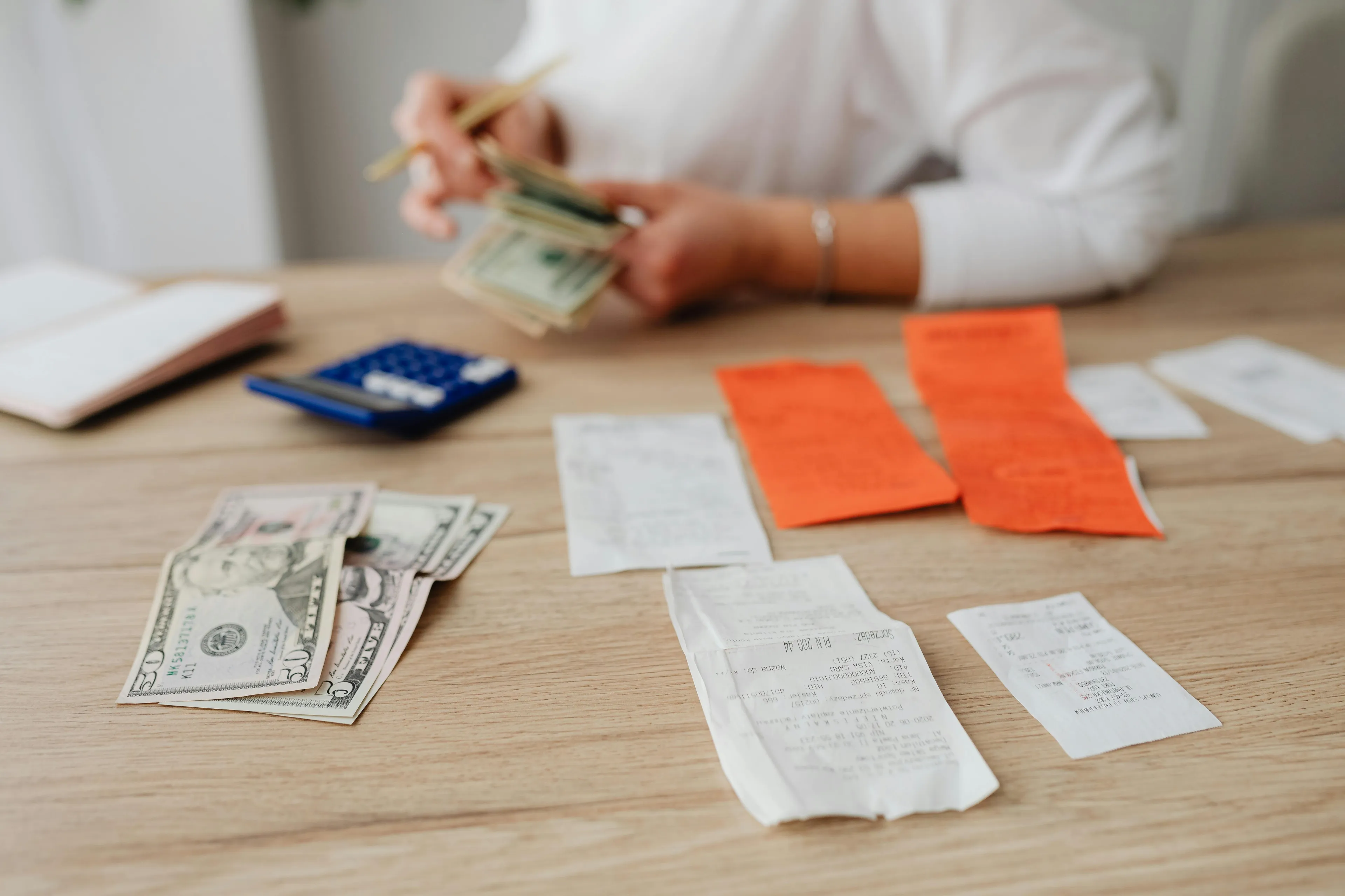 Person counting money with calculator and receipts on table tracking fixed expenses in monthly budget planning