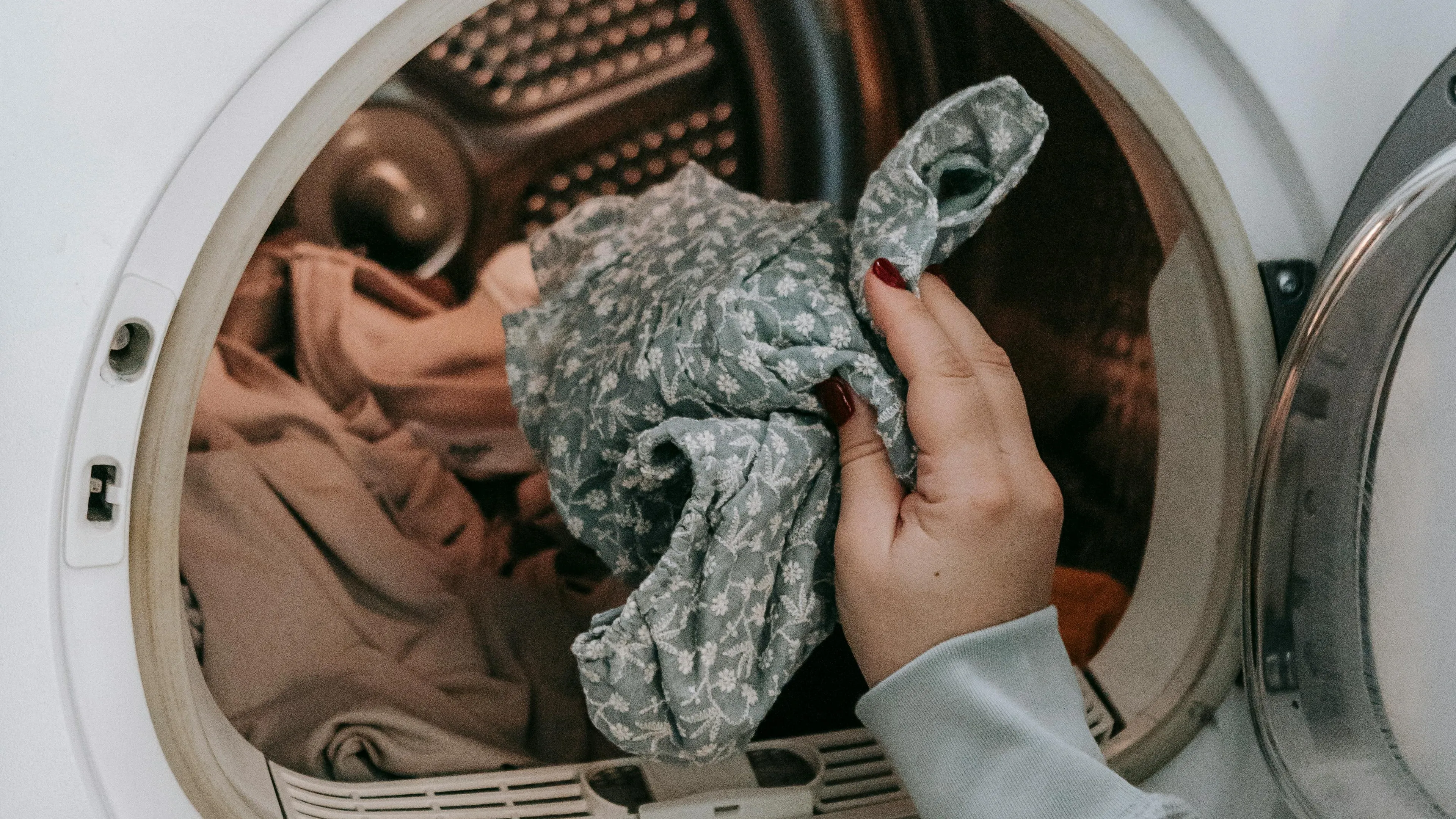 Hand holding patterned clothing inside front-load washing machine to prevent bright or dark clothes fading in wash.