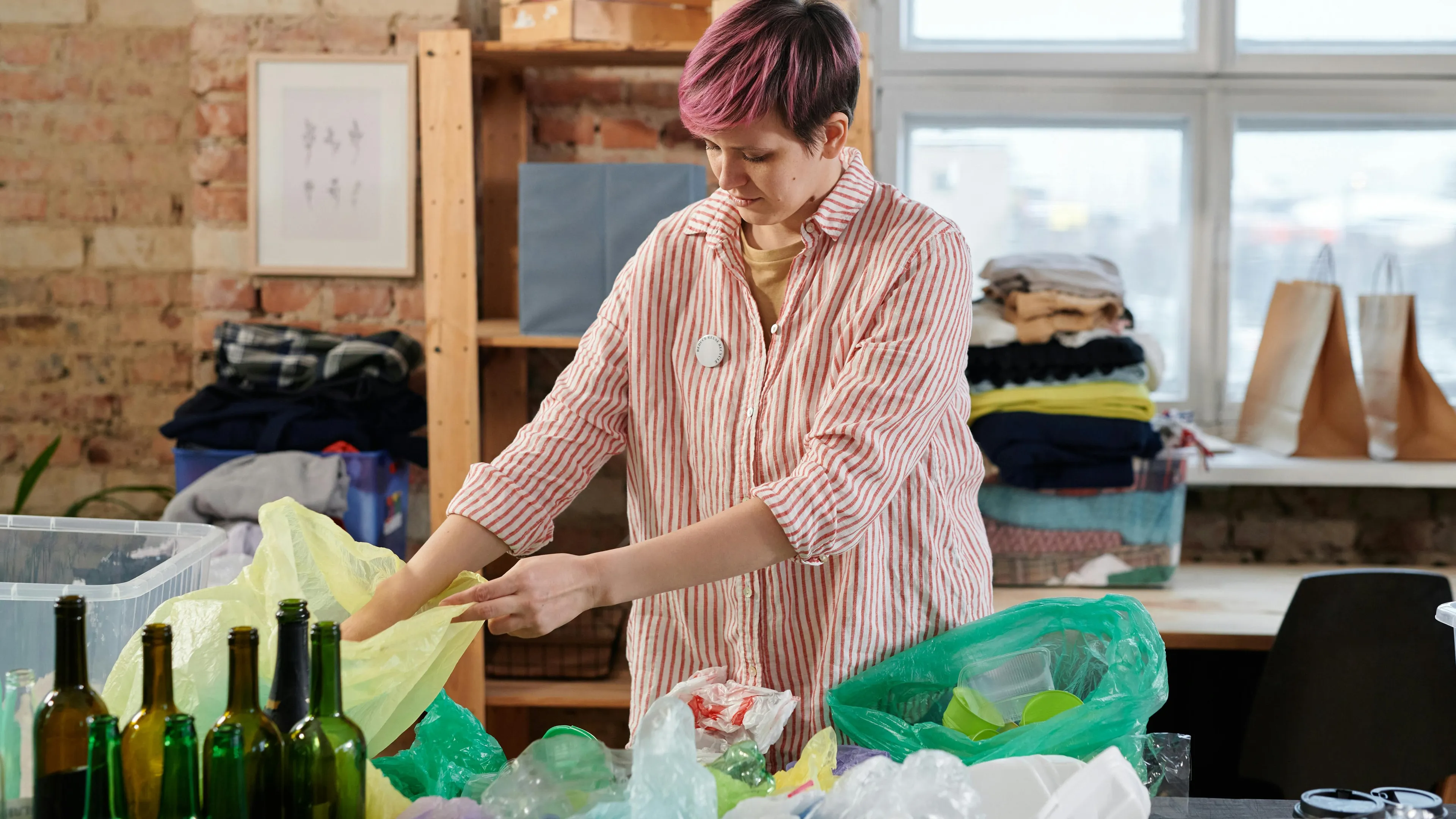 Person sorting recyclable glass bottles and plastic bags in an indoor recycling setup for infinitely recyclable items.