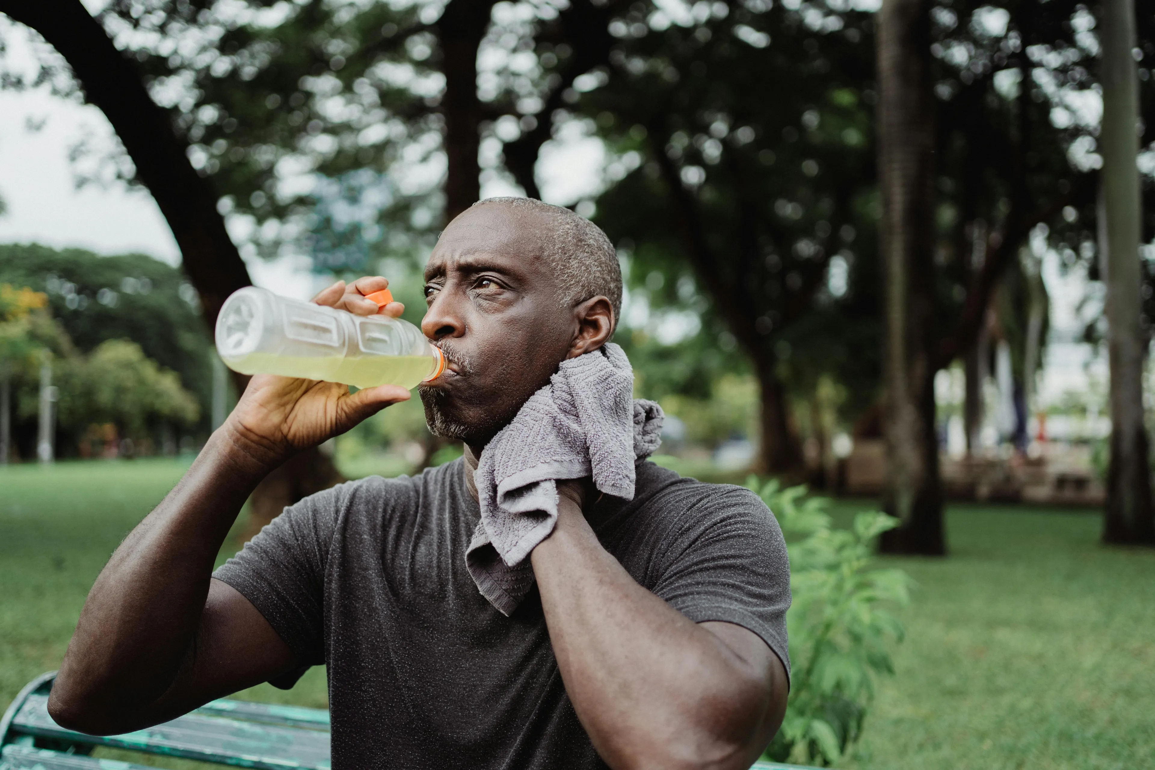 Middle-aged man drinking electrolyte drink and wiping sweat outdoors, highlighting the role of electrolytes in the human body.