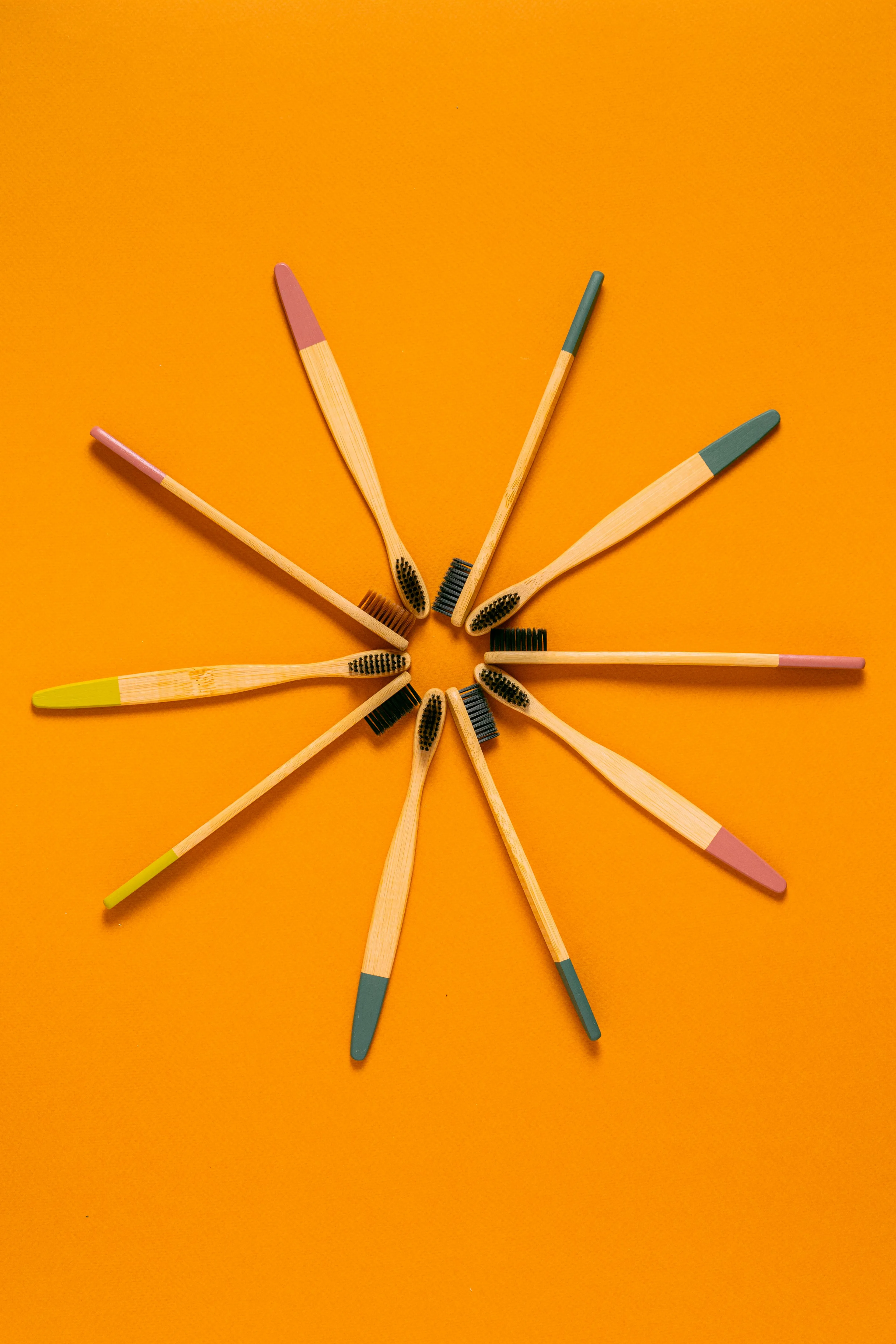 Bamboo toothbrushes with colored tips arranged in a circle on an orange background representing when to change your toothbrush.