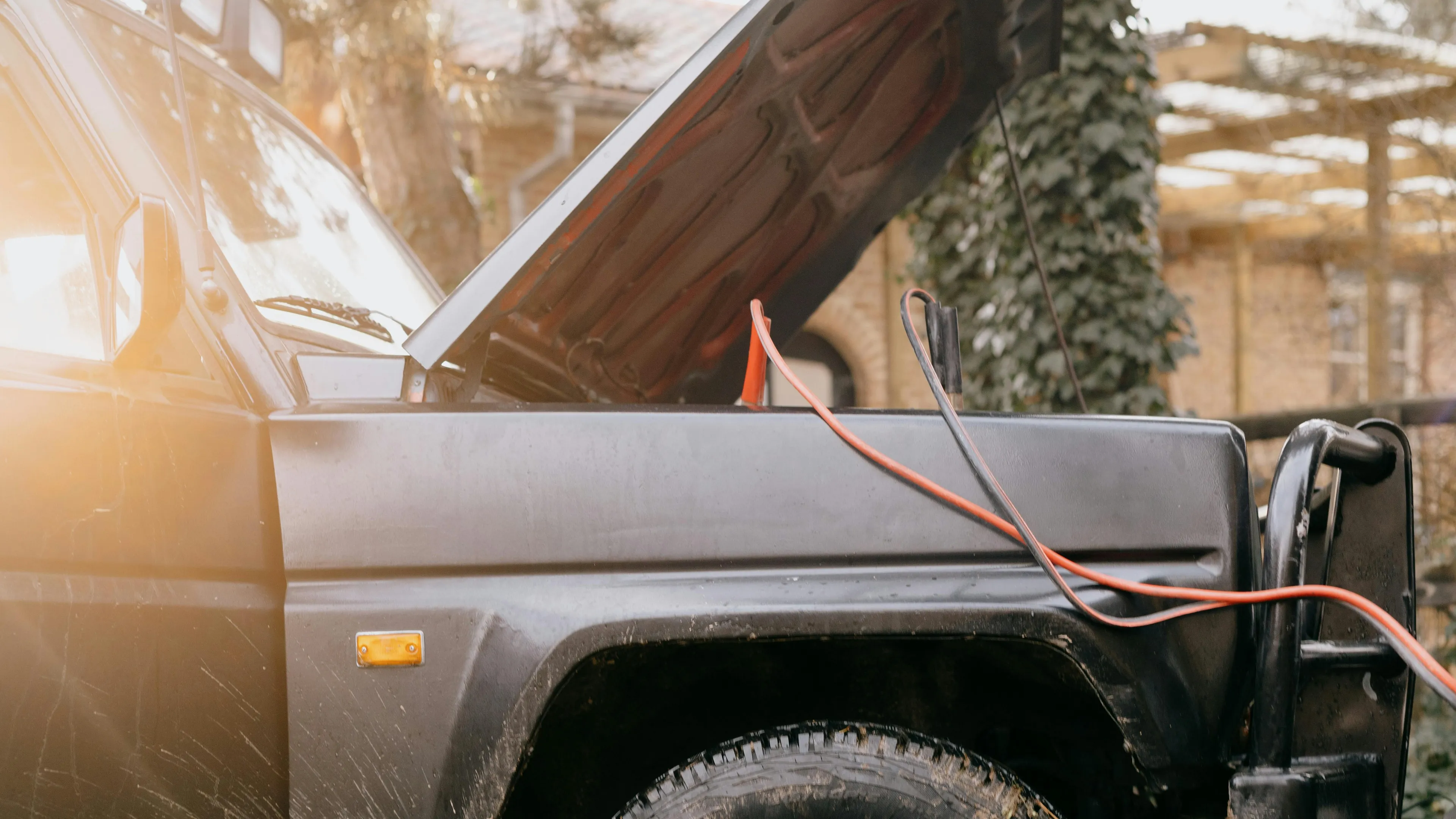 Black SUV with open hood and red and black cables connected, illustrating jump start with drained battery process.