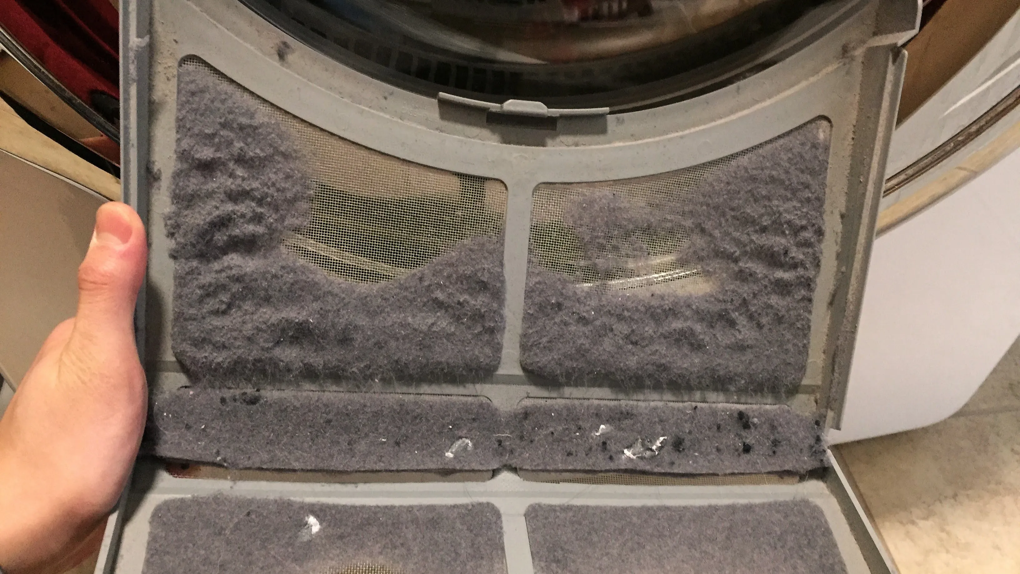 Hand holding a dryer lint trap clogged with lint, illustrating how often the lint trap of a dryer should be cleaned.