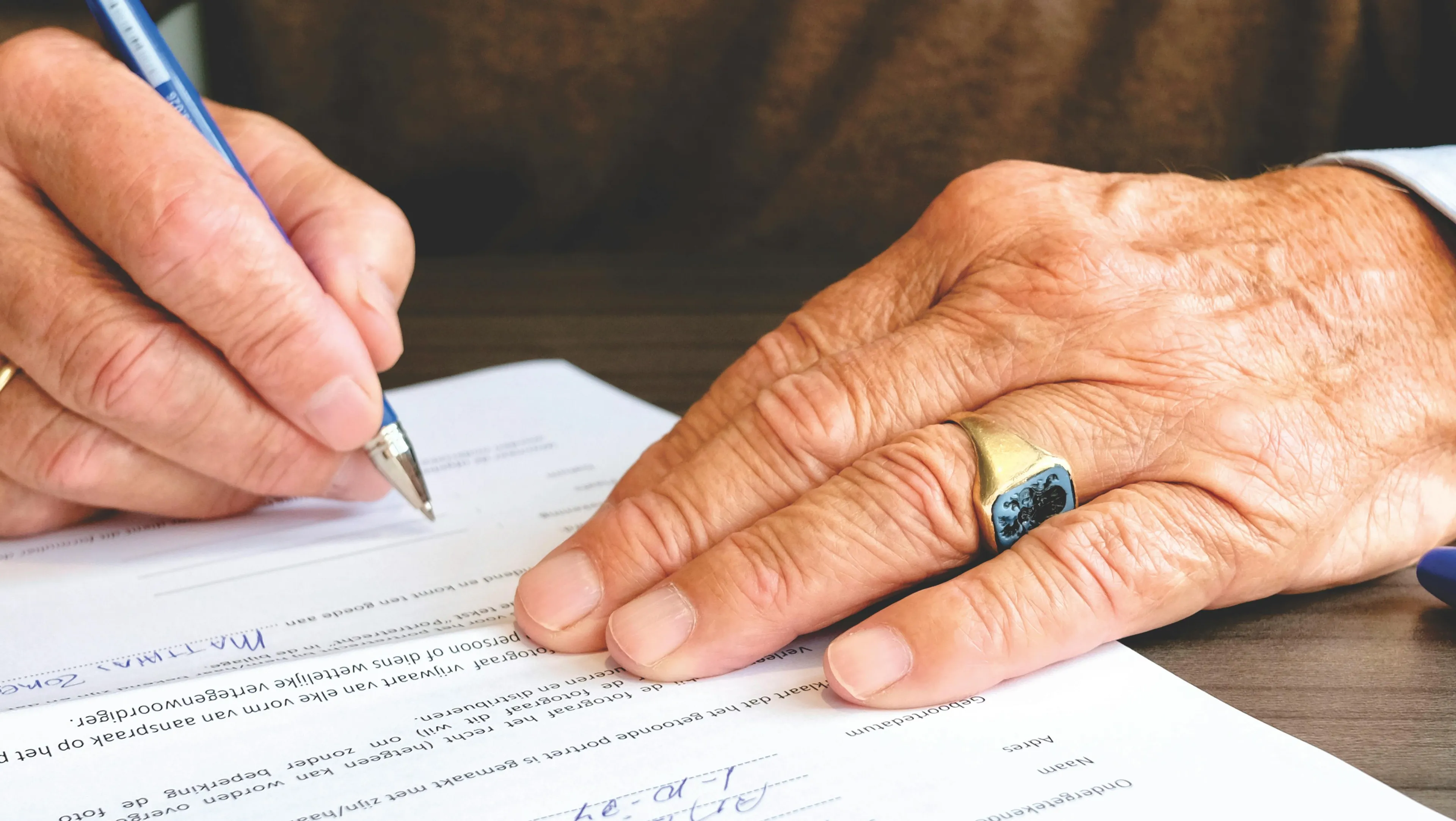 Close-up of elderly hands signing a legal document related to asset distribution without a last will and testament.