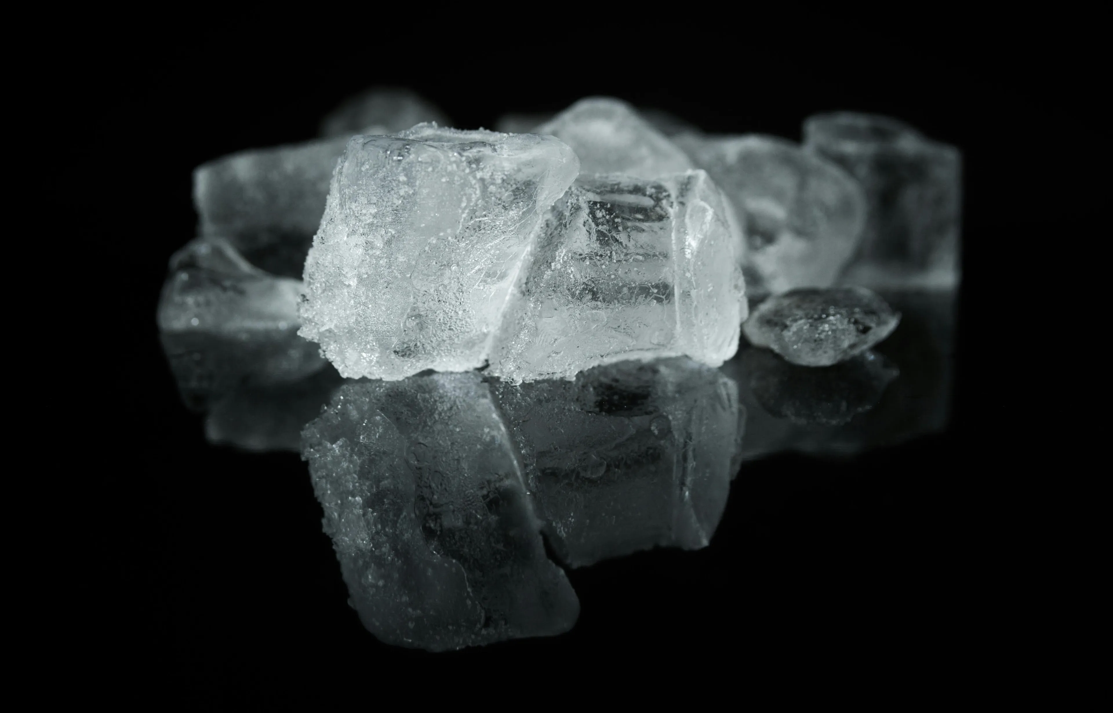 Close-up of melting ice cubes on a reflective surface illustrating the science process of ice shrinking over time.