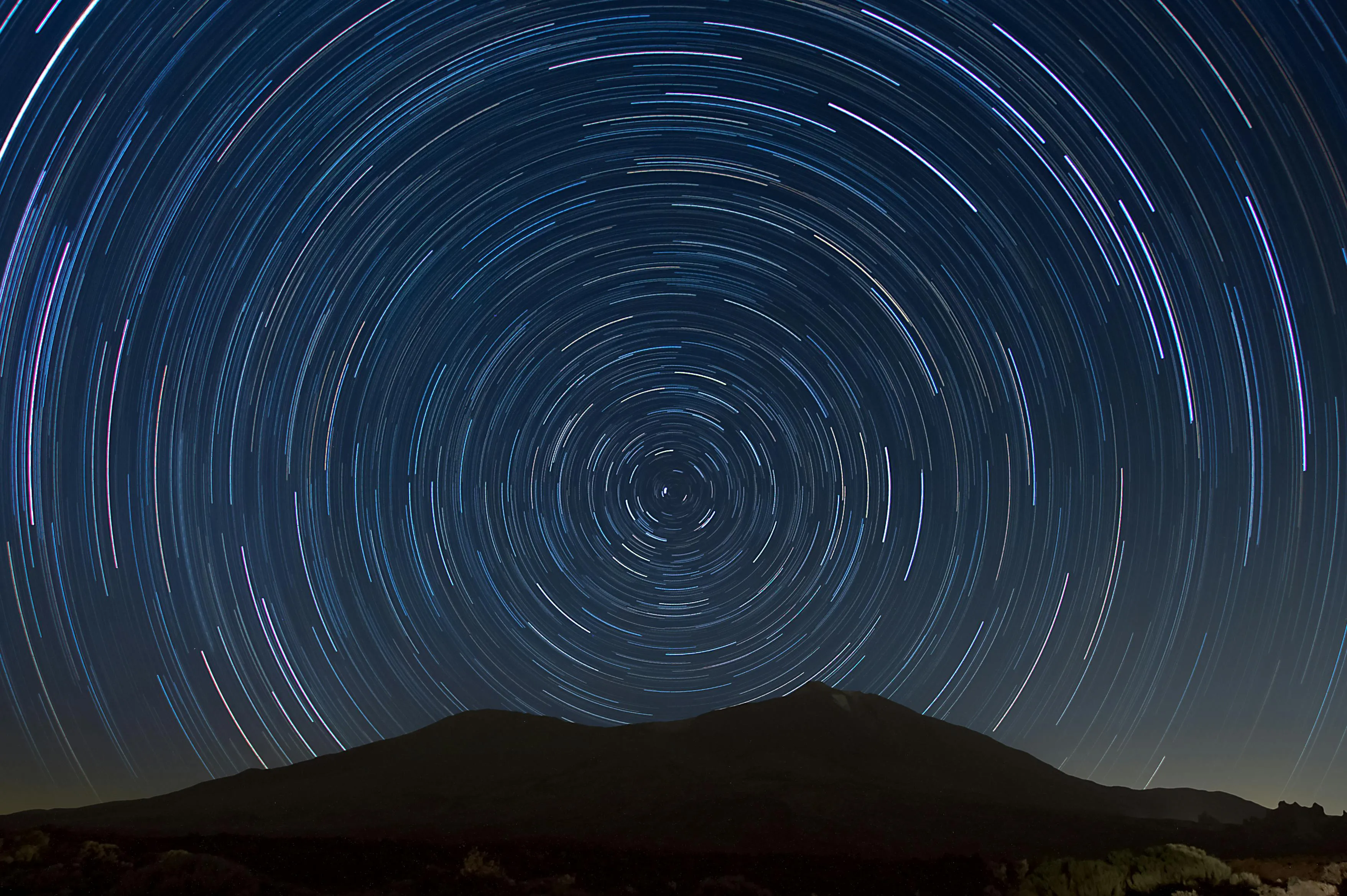Long exposure photo of star trails circling above a mountain, illustrating a planet's path around a star orbit concept.