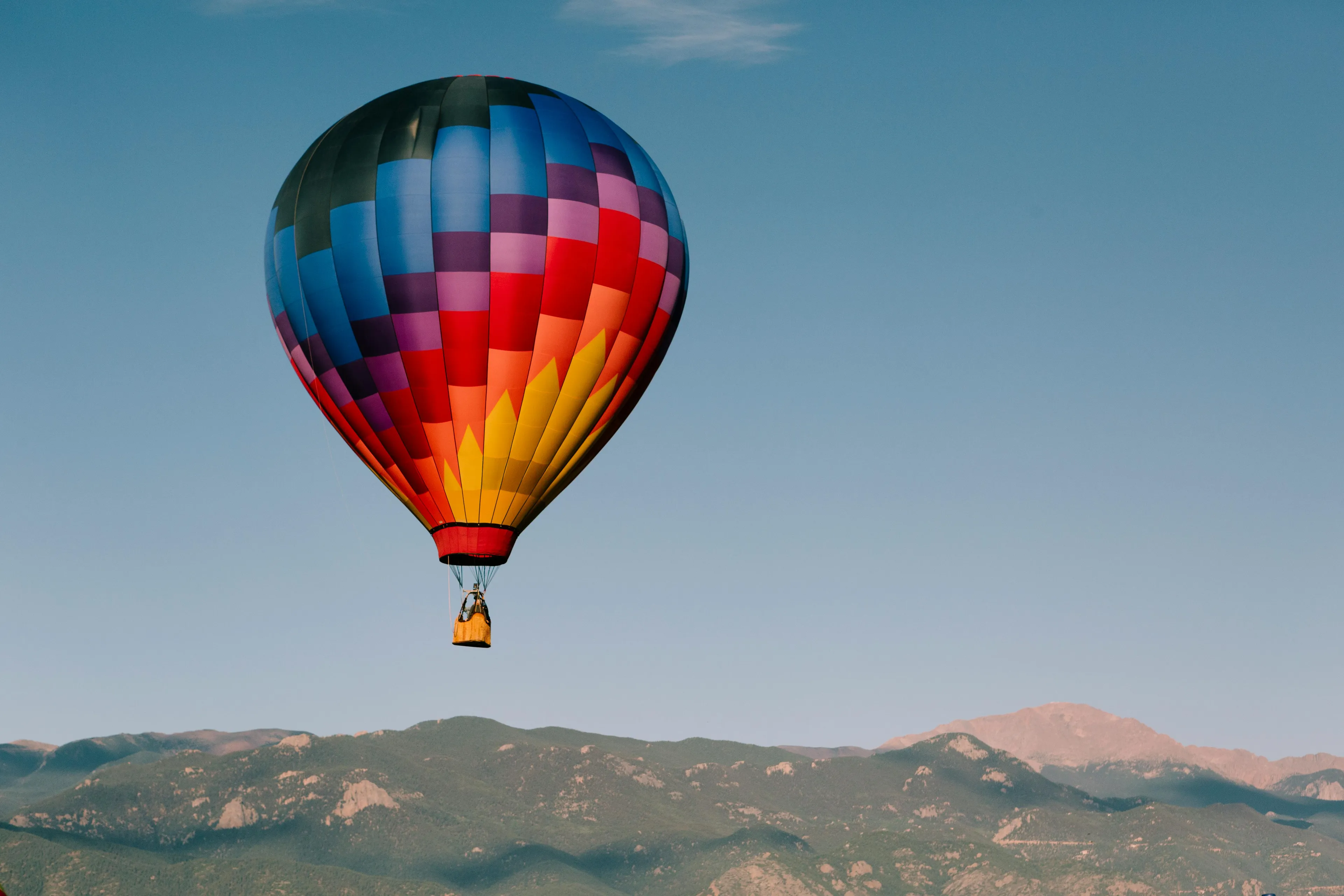 Colorful hot air balloon floating above mountains against a clear sky illustrating warm air balloon temperature effects indoors.