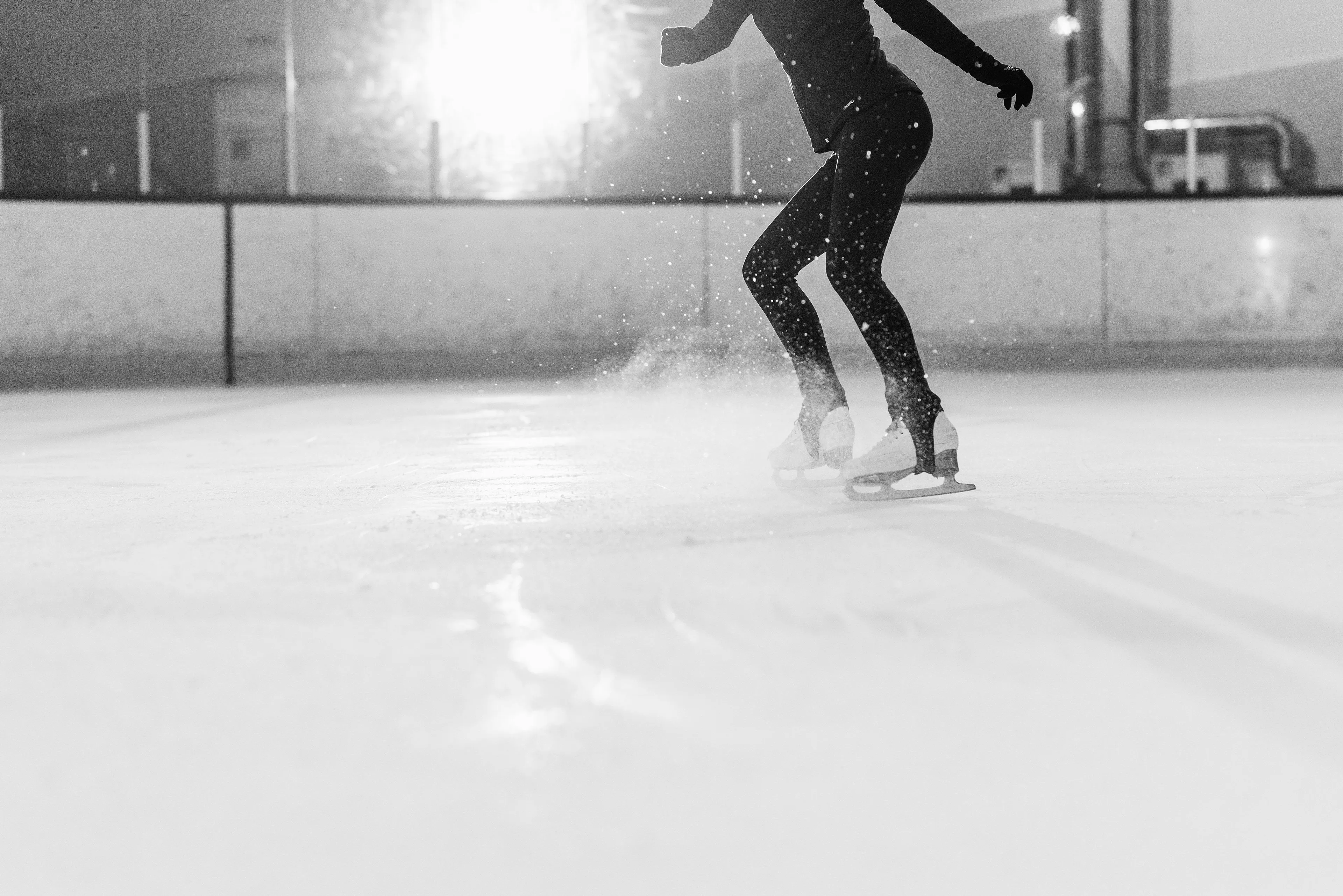 Ice skater jumping and tucking legs mid-air on ice rink, demonstrating the science behind spinning faster in motion.