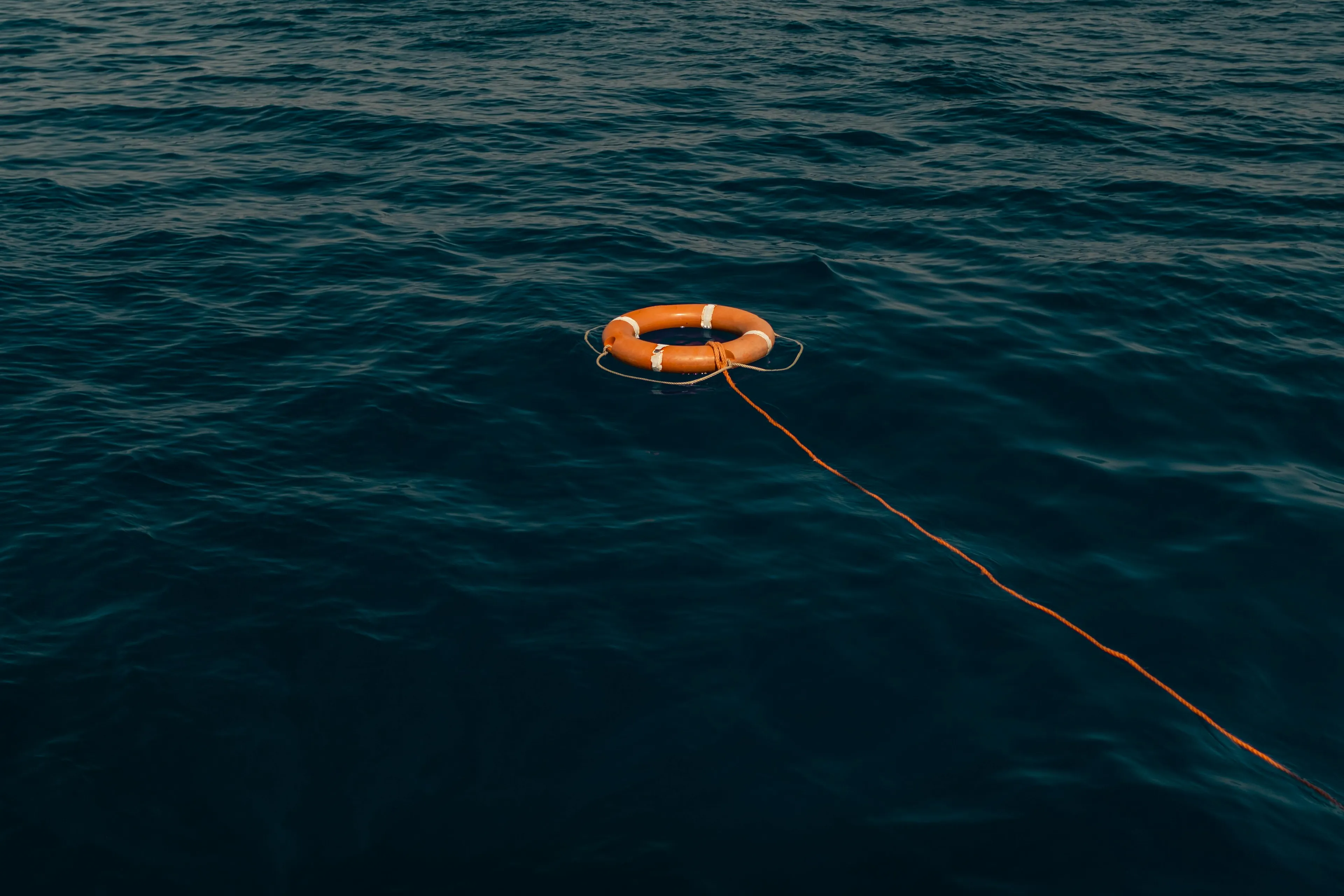 Orange life buoy floating on dark blue water, illustrating factors affecting buoyant force on submerged objects.