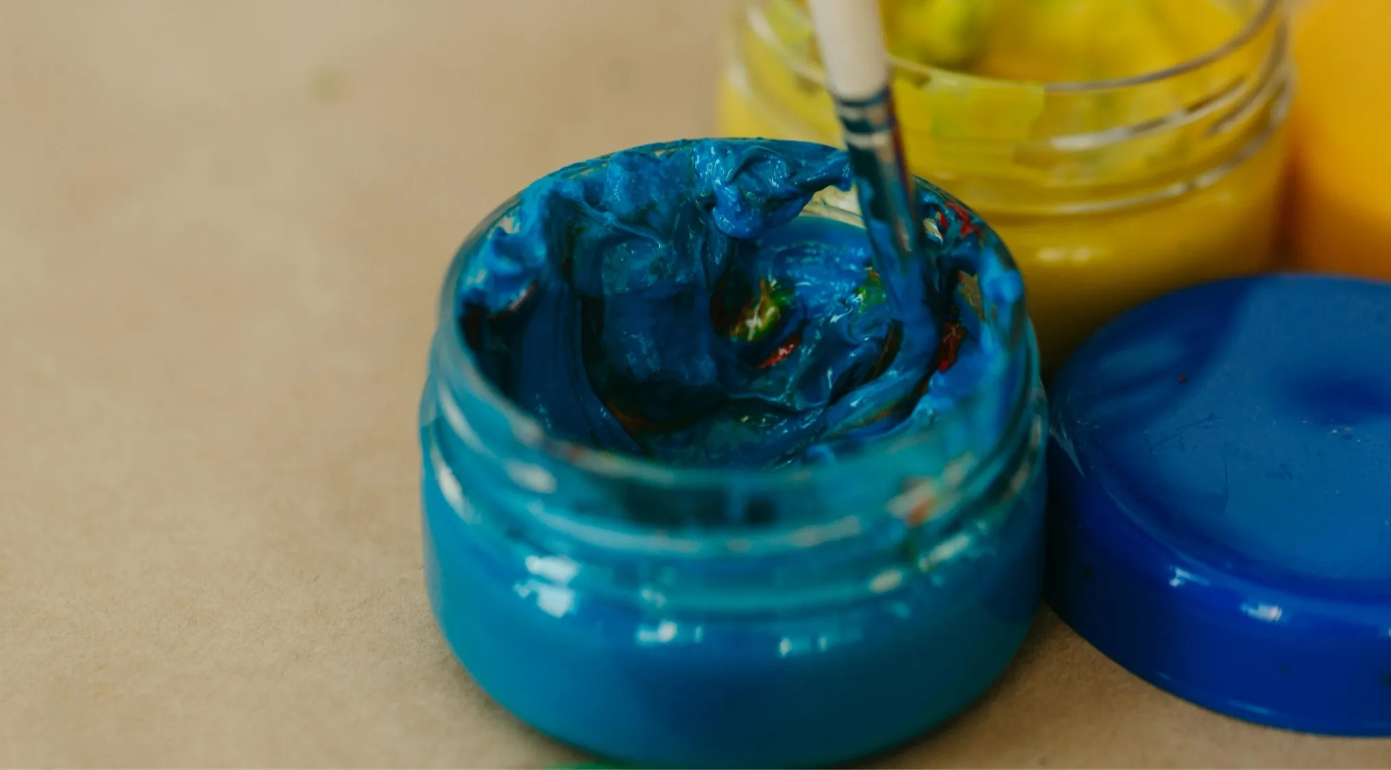 Close-up of blue and yellow paint jars with brush mixing colors for an easy-to-hard general knowledge quiz question.