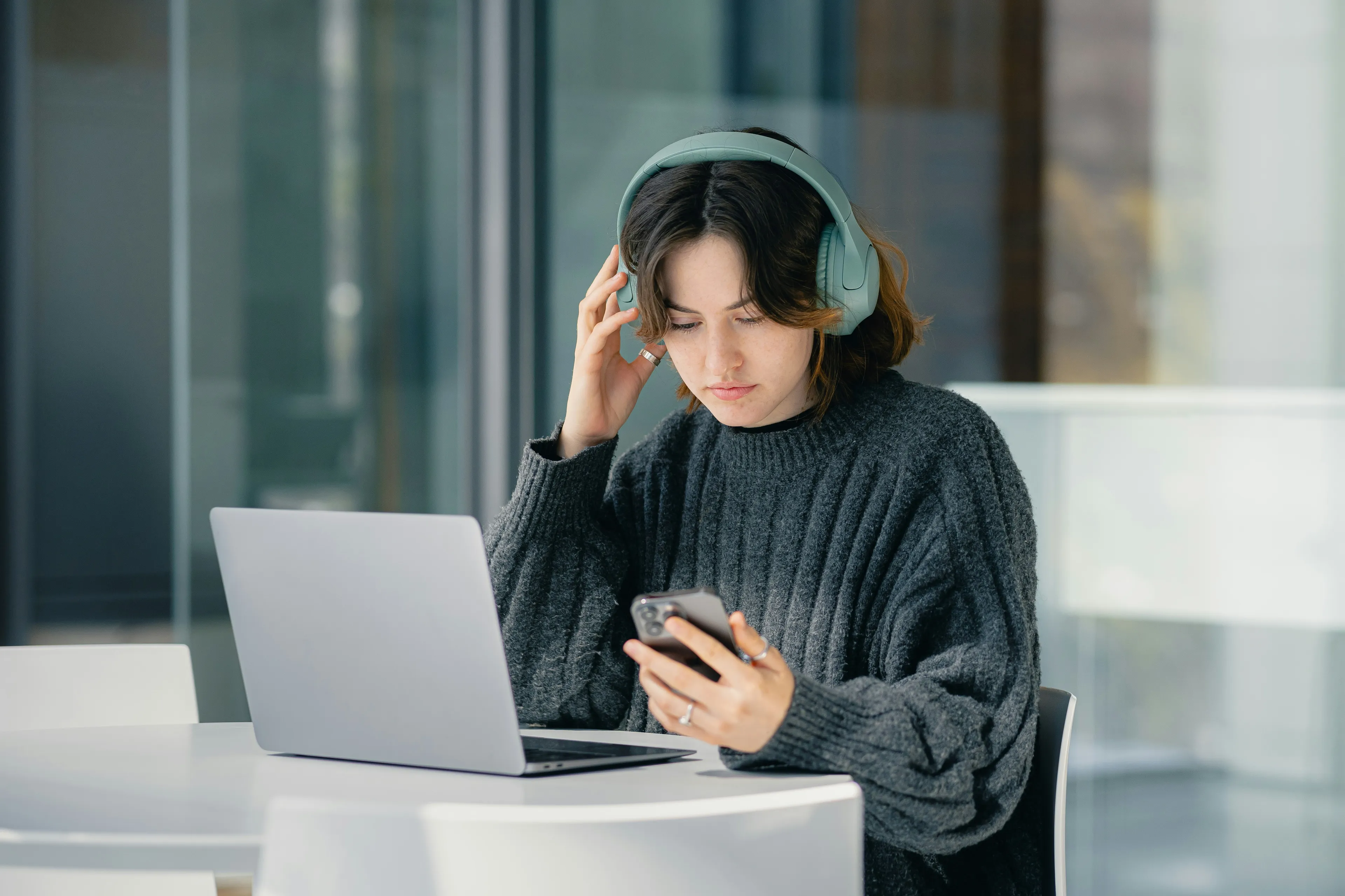 Young woman wearing headphones using smartphone and laptop, focused on an easy-to-hard general knowledge quiz.