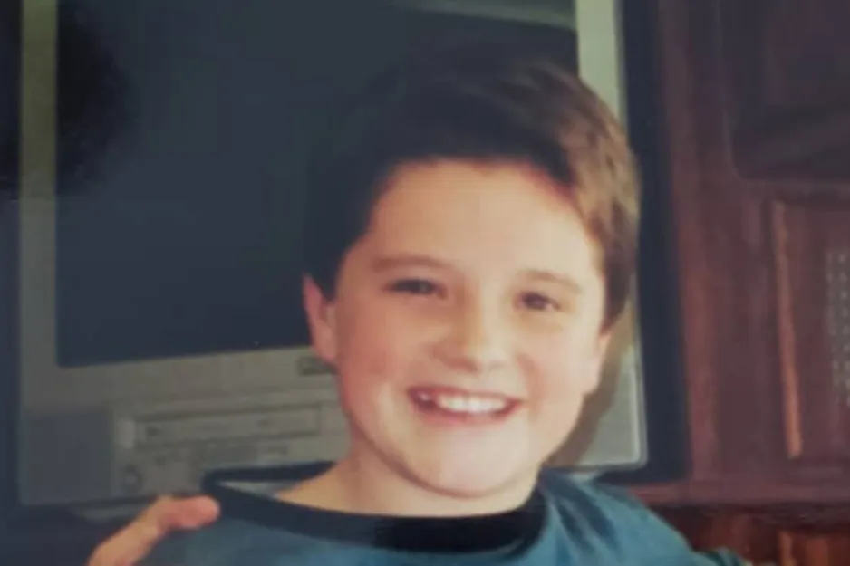 Young boy smiling in front of a vintage computer, challenging viewers to spot Ryan Reynolds in the image.