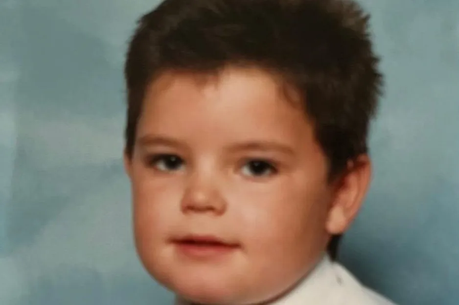 Young boy with short dark hair wearing a white shirt posing for a portrait photo against a blue background.