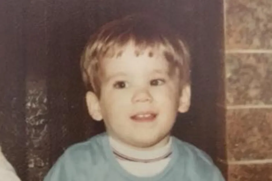 Toddler wearing a blue shirt sitting indoors with a curious expression, main focus on Ryan Reynolds childhood photo.