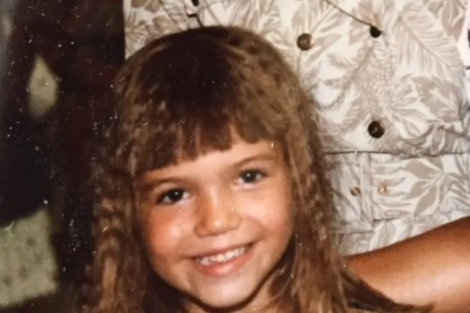 Young girl smiling with crimped hair and bangs in a close-up photo, featuring Allison Williams as a child.