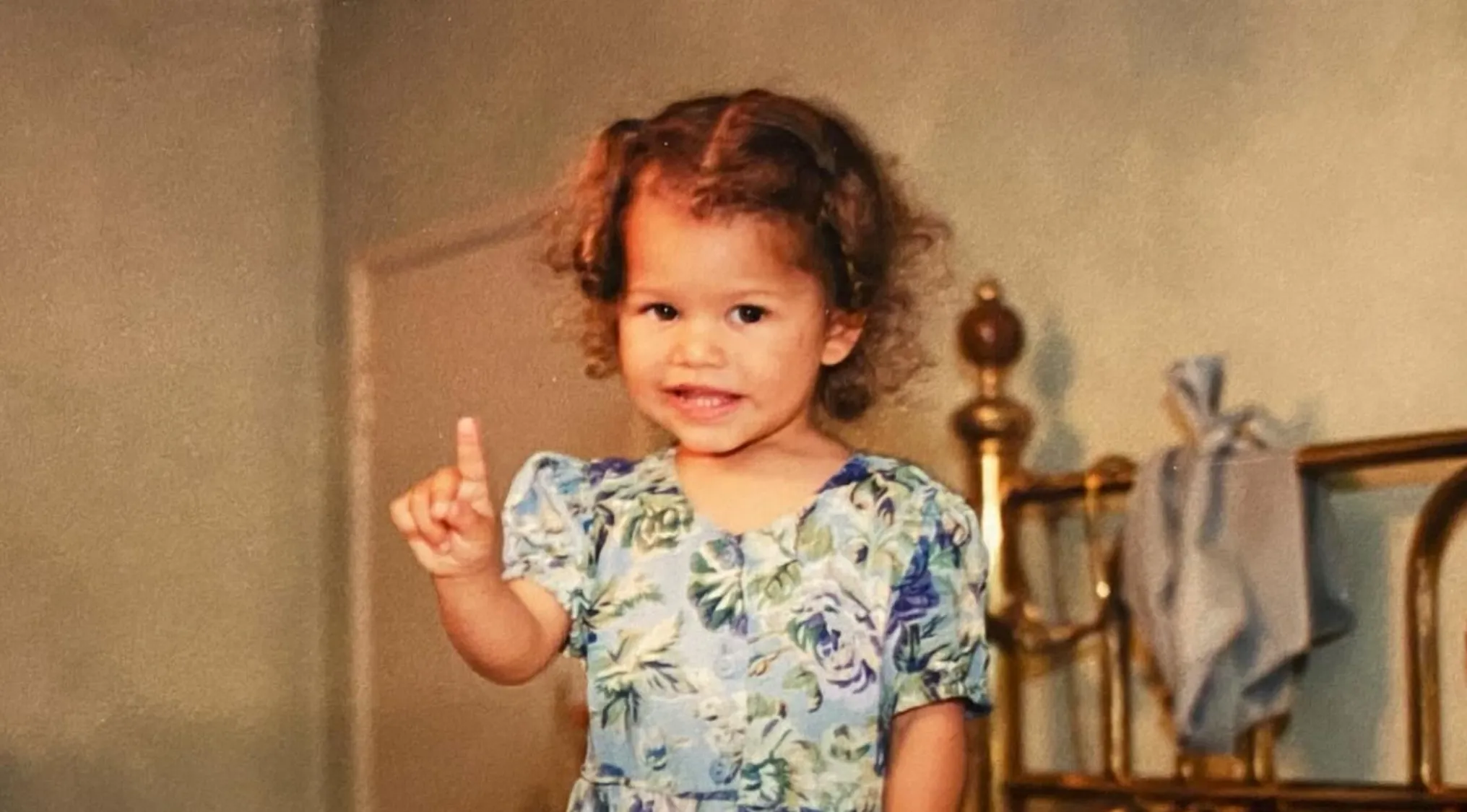 Toddler girl with curly hair wearing a floral dress posing indoors in a vintage setting for celebrities as kids photos.