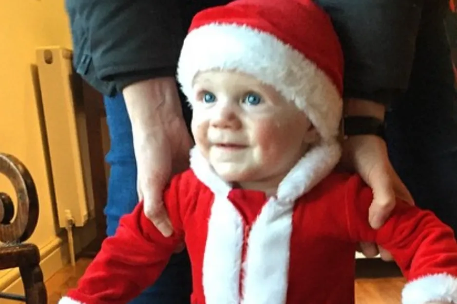 Young child dressed in a red and white Santa outfit, smiling with blue eyes, representing Jimmy Fallon as a youngster.