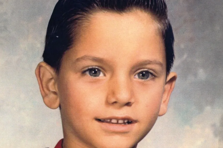 Young Jimmy Fallon as a child with slicked-back hair and a red shirt, smiling for a school portrait photograph