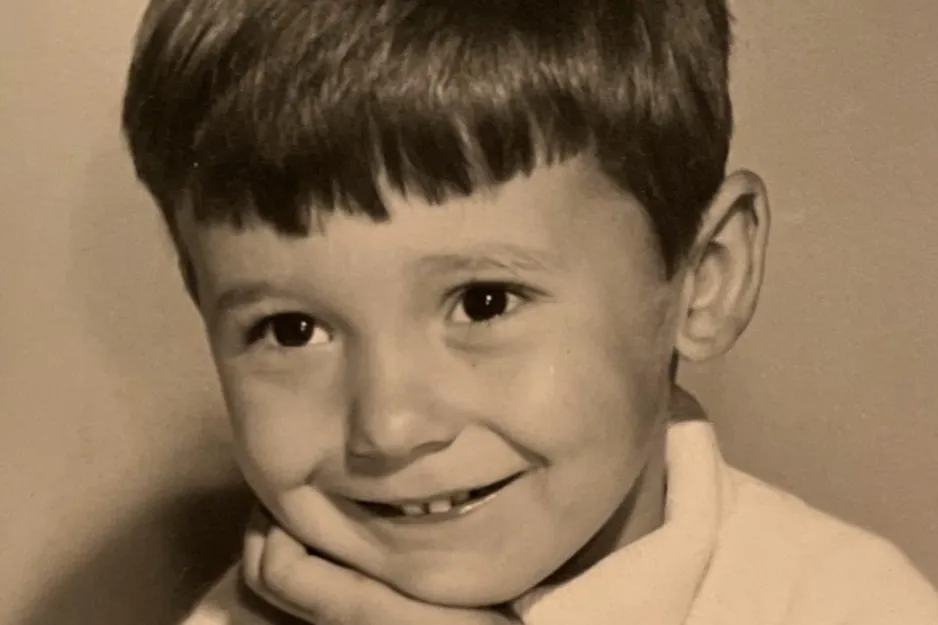 Young boy with short hair smiling gently, resting head on hand in a vintage black and white photo.
