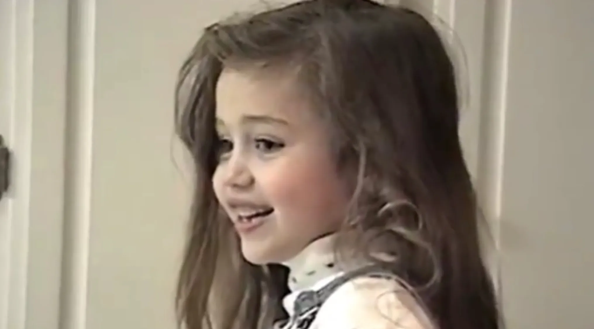 Young girl smiling indoors, showcasing a charming look in a vintage-style outfit from celebrities as kids.