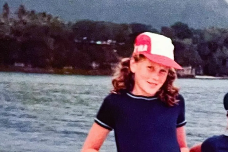 Child wearing a red and white cap and navy shirt smiling by a lake, a nostalgic image related to Adele identification.